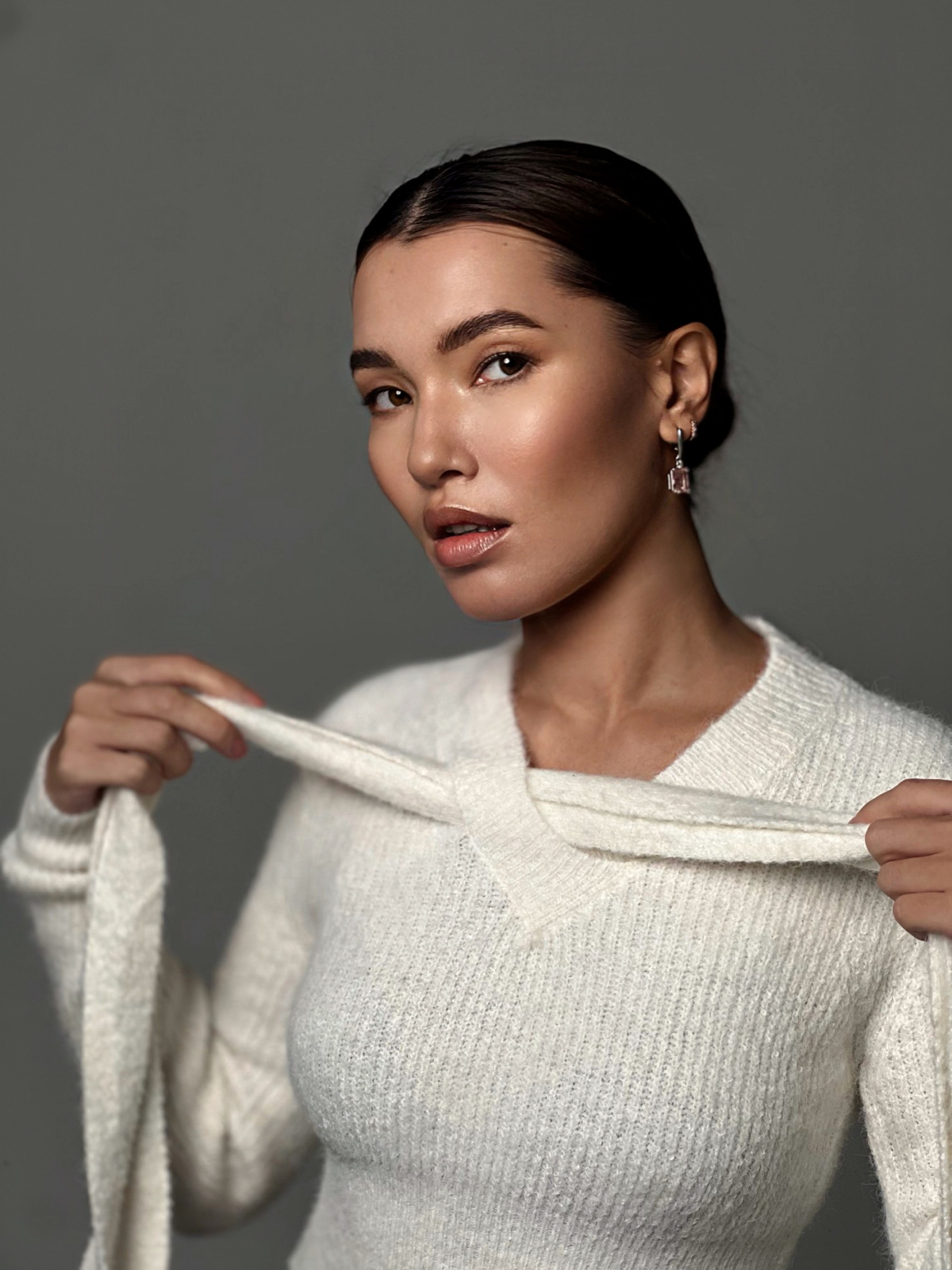 Девушка азиатской внешности позирует в белом вязаном свитере