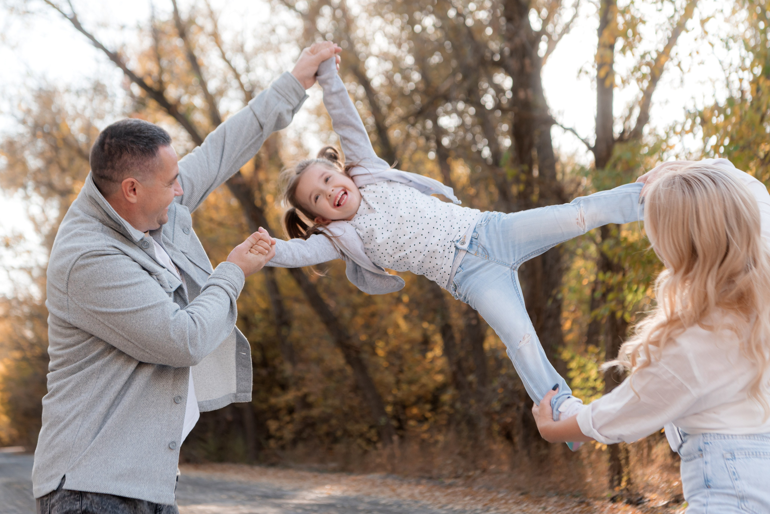 Живые эмоции на семейной фотосессии - родители играют с ребёнком подбрасывая дочку за руки и ноги.