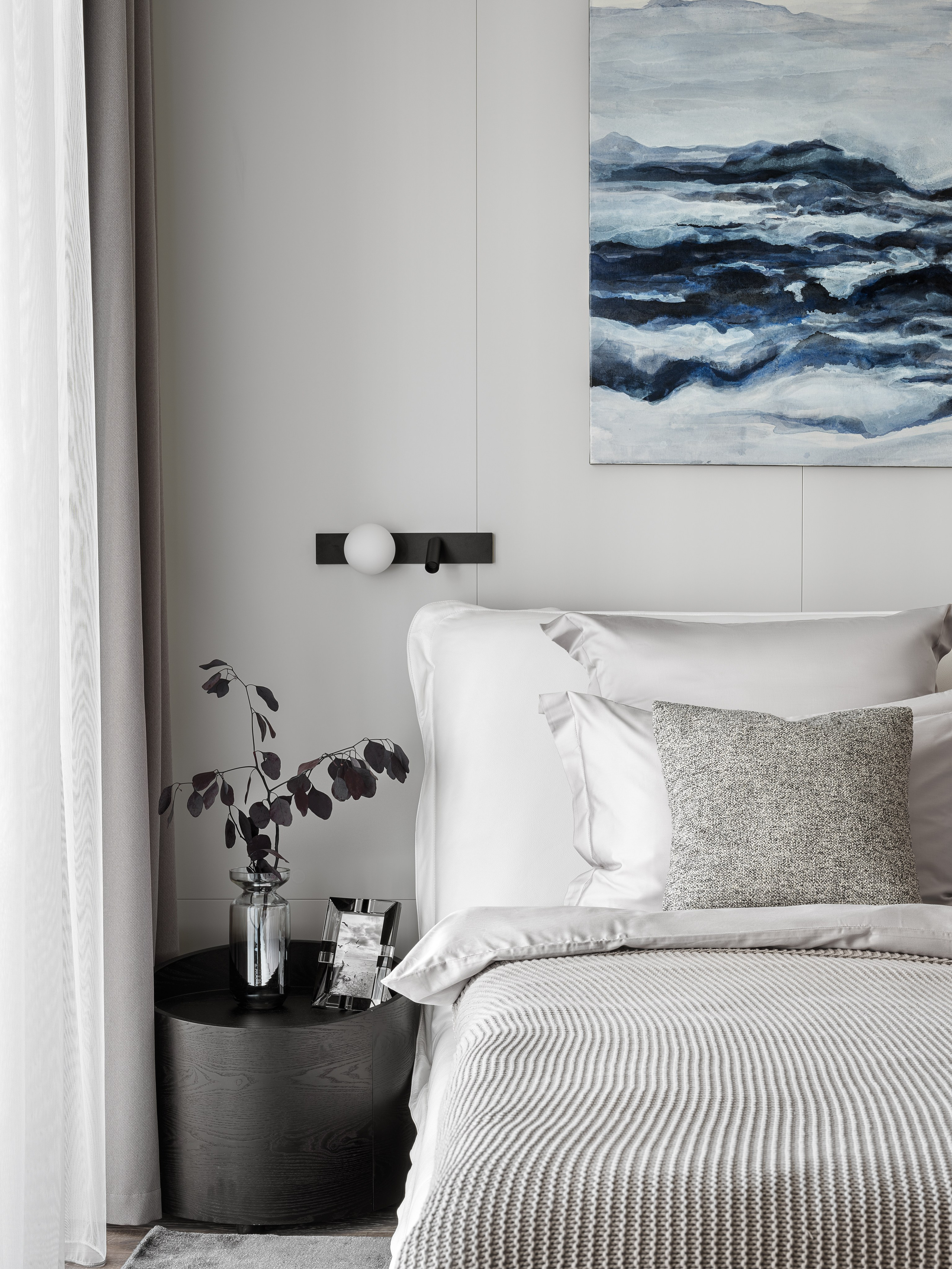 Современный интерьер спальни в Сочи с акцентом на минималистичное оформление: мягкая кровать с серыми подушками, тумба с вазой и картина в морской гамме. Дизайн: Ренат Байчуков и Алеся Кириенко, стилист Екатерина Ракитина, фотограф Сергей Денисенко.