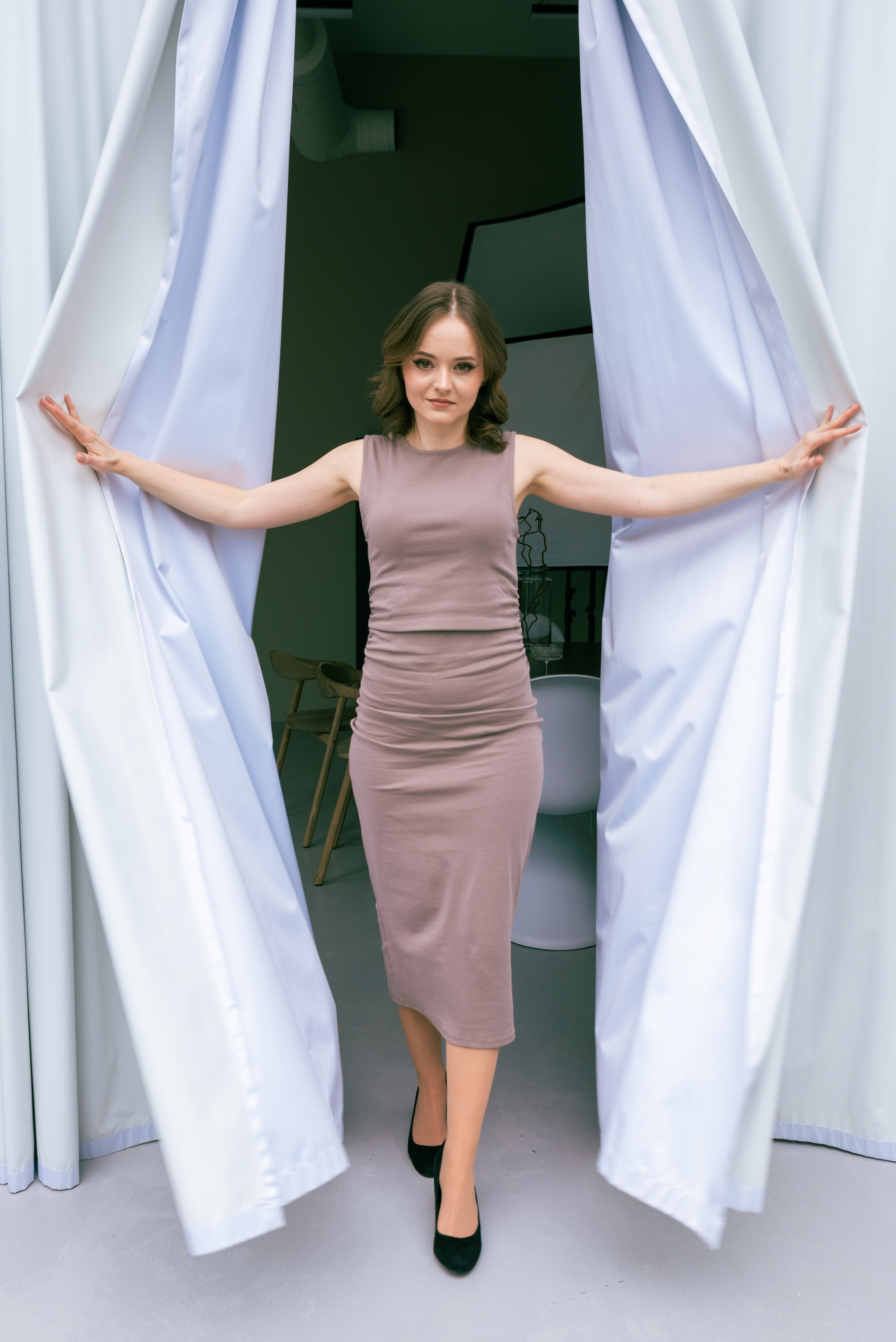 Девушка проходит между двух белых занавесок раздвигая их в стороны.