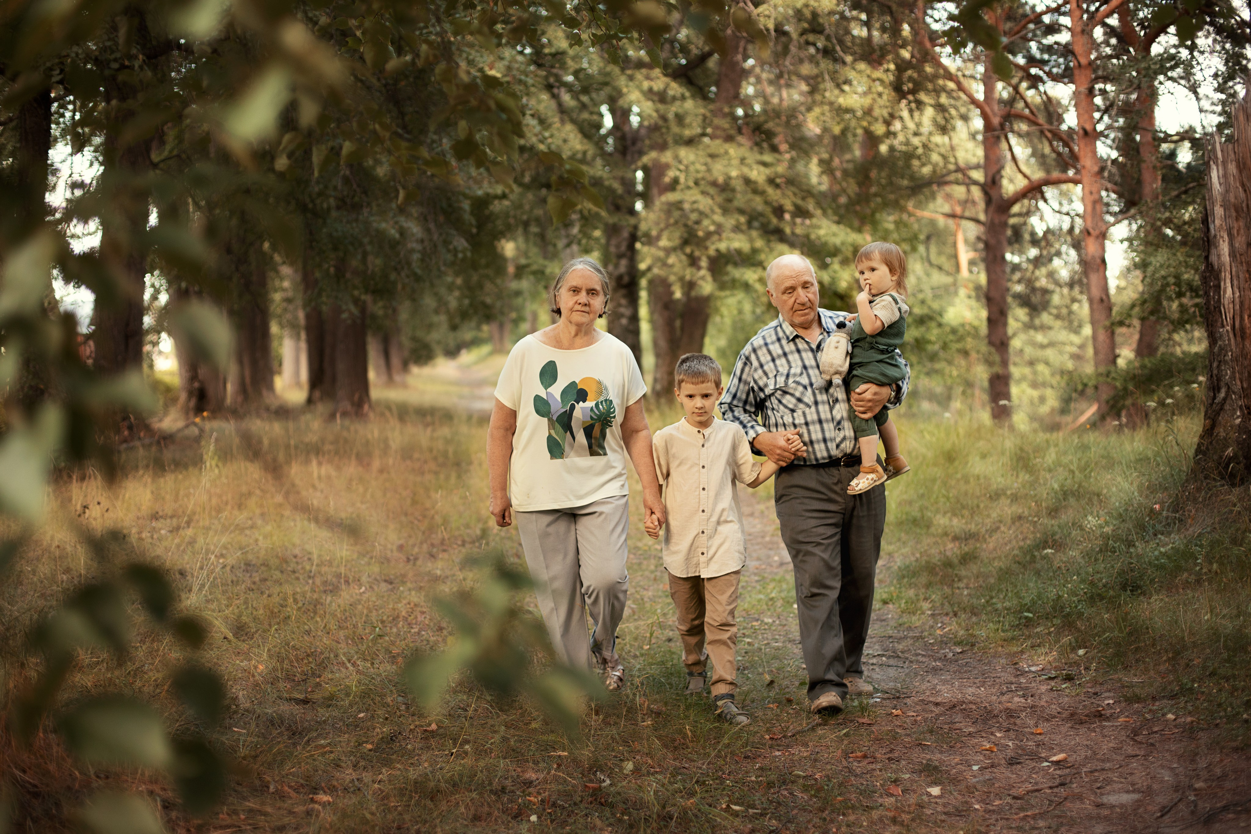 Бабушка и дедушка идут с внуком и внучкой в летнем парке