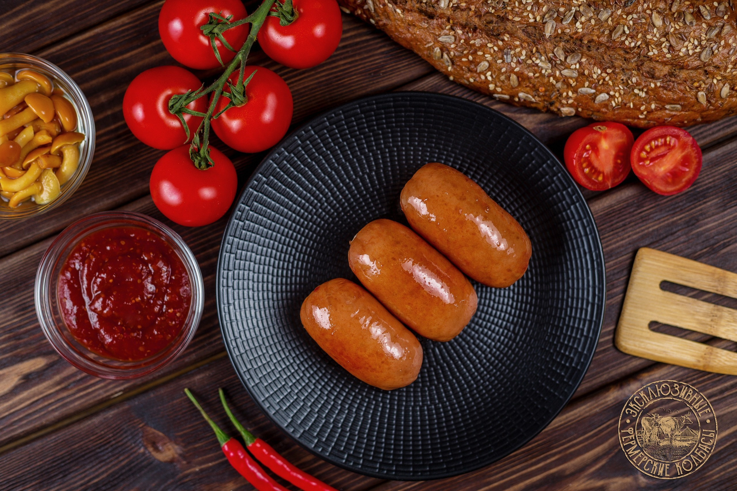Черная тарелка с сардельками на деревянном фоне