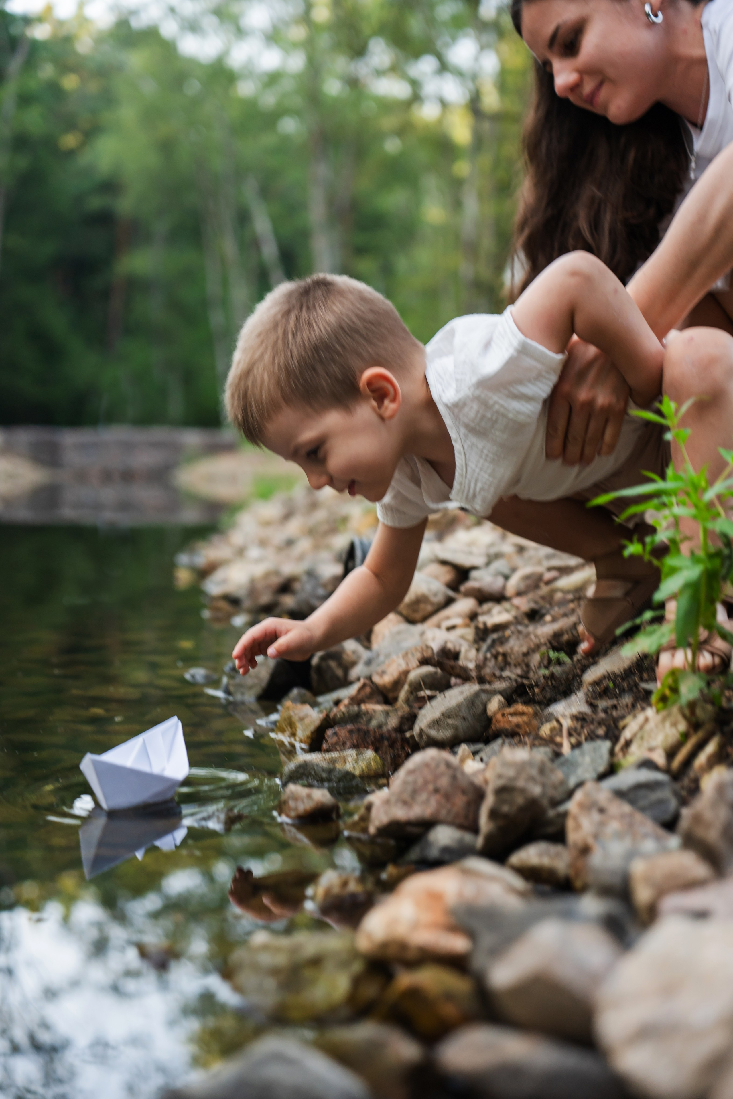 ребенок запускает бумажный кораблик в воду