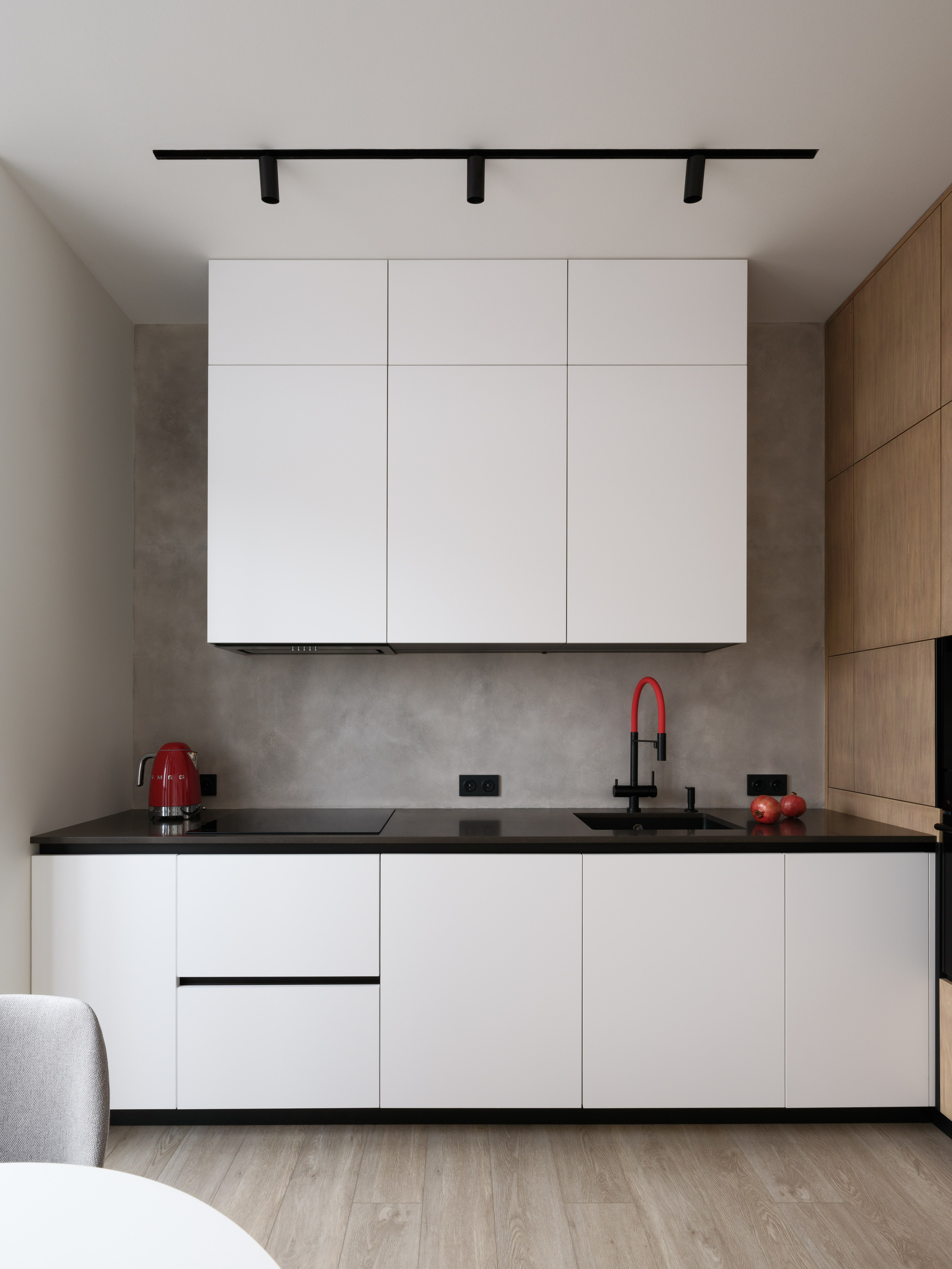 Современная кухня в минималистичном стиле с белыми шкафами, черной столешницей и красным смесителем. Автор проекта — дизайнеры Евгения Княжева и Владлена Привалова, фотограф Сергей Денисенко