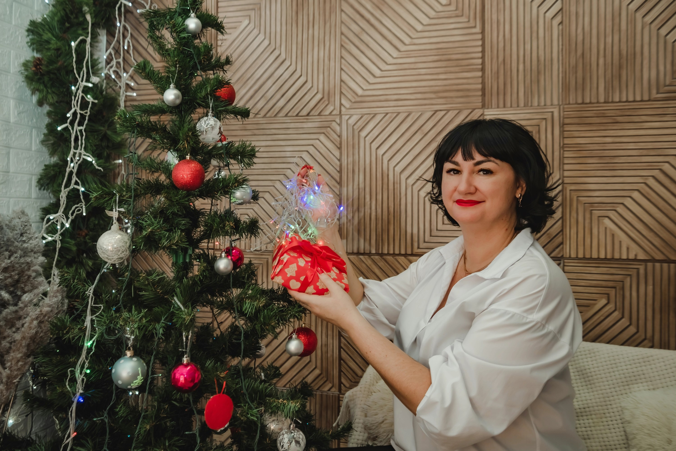 На фото девушка с подарком около елки.