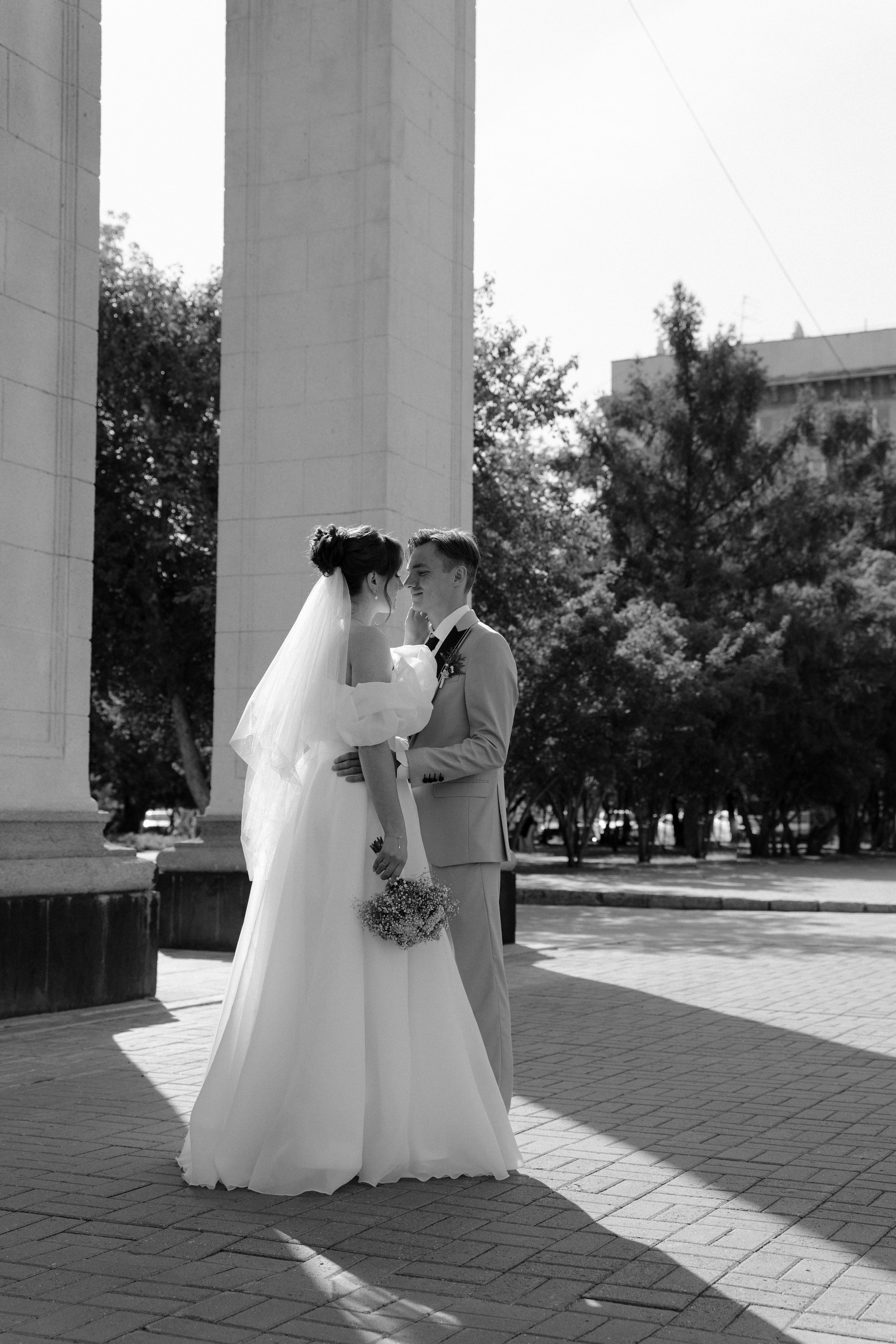 Молодожены у колонн театра стоят на улице летом в городе