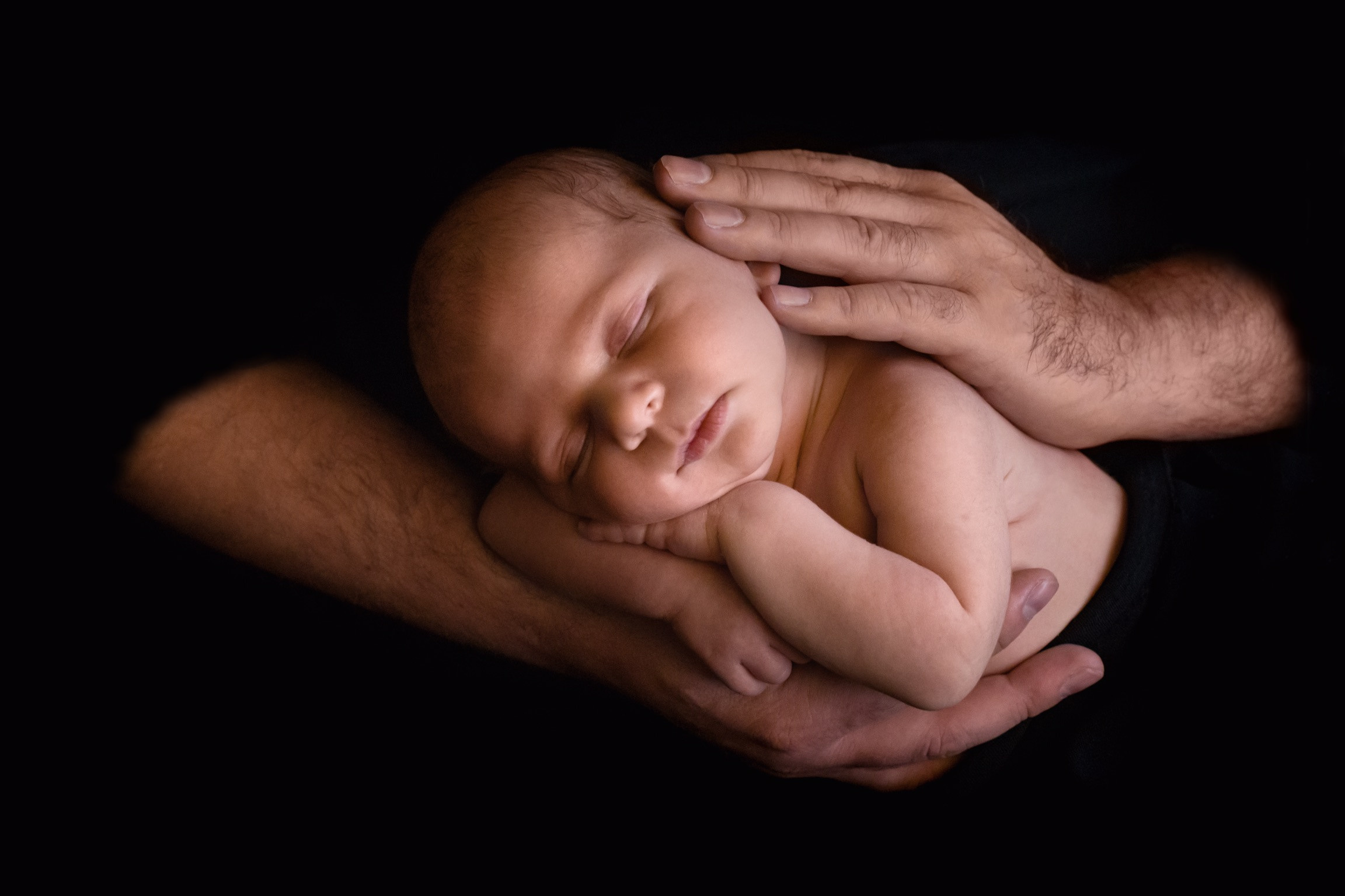 отец держит в руках новорожденного сына на черном фоне