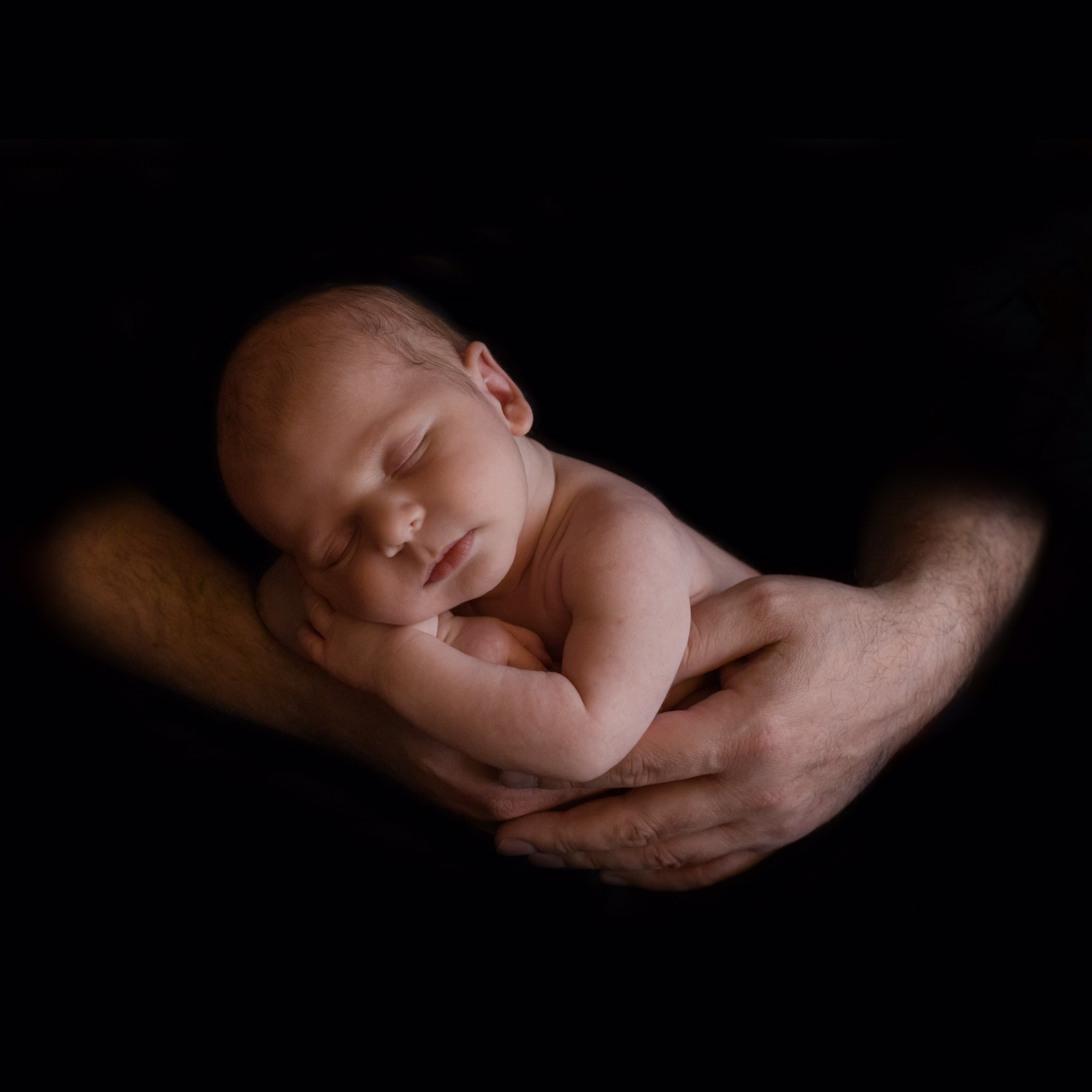 младенец в папиных ладонях на черном фоне