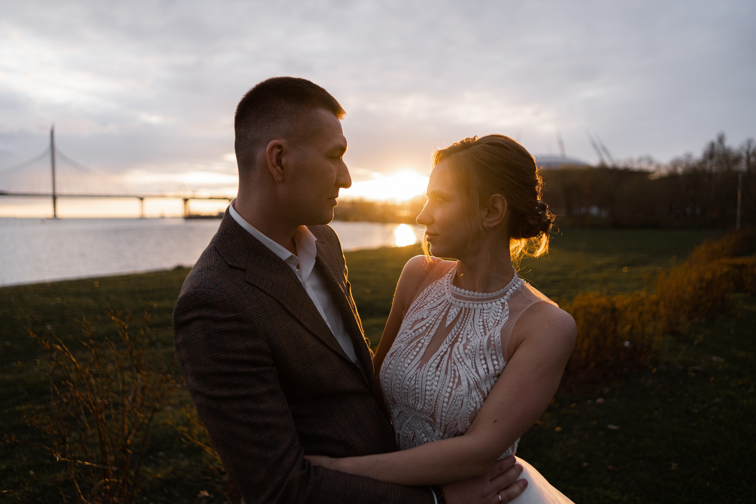 Жених и невеста стоят рядом на фоне моря и заходящего солнца в Санкт-Петербурге