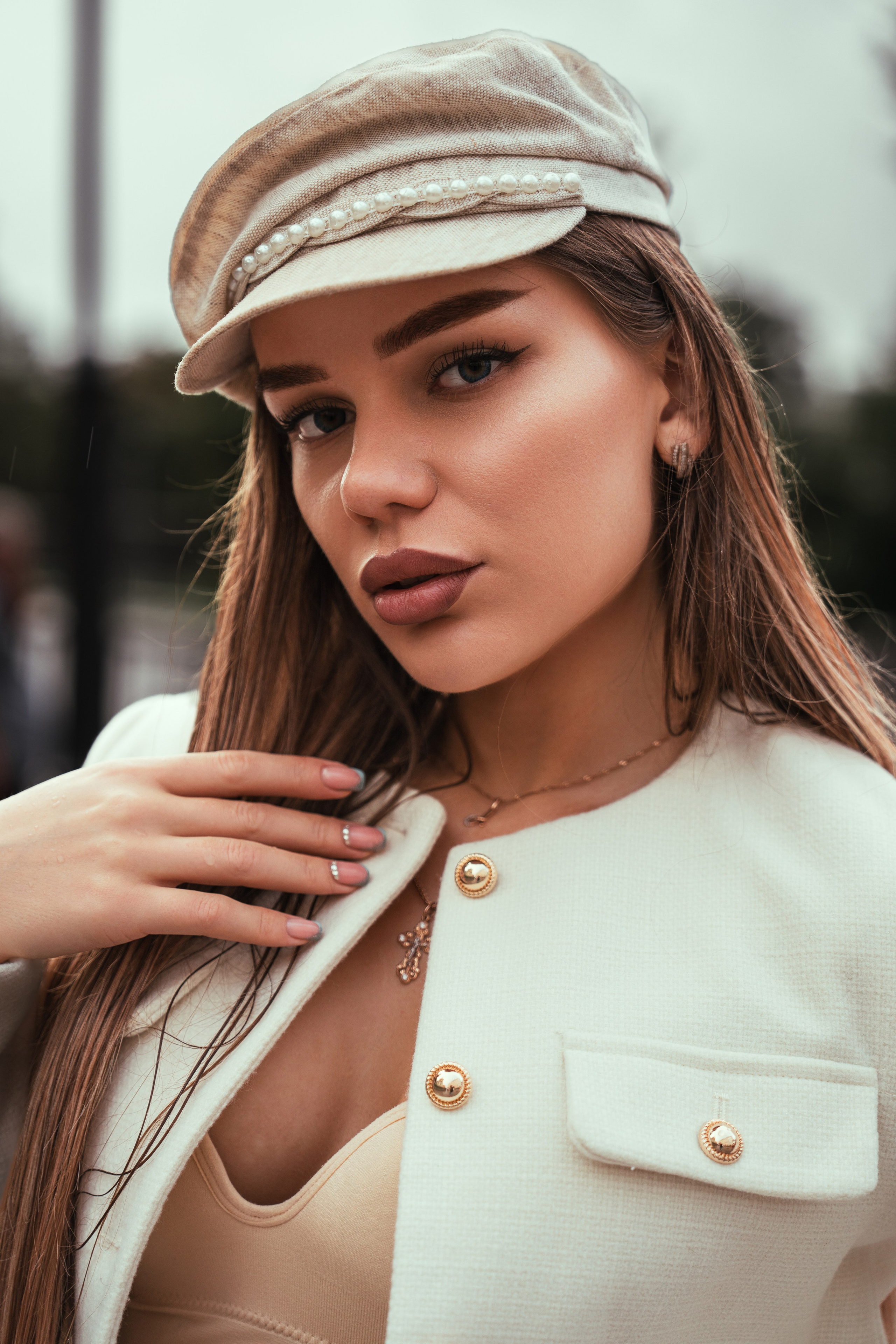 красотка в шляпке и кремовом пиджаке позирует на улице