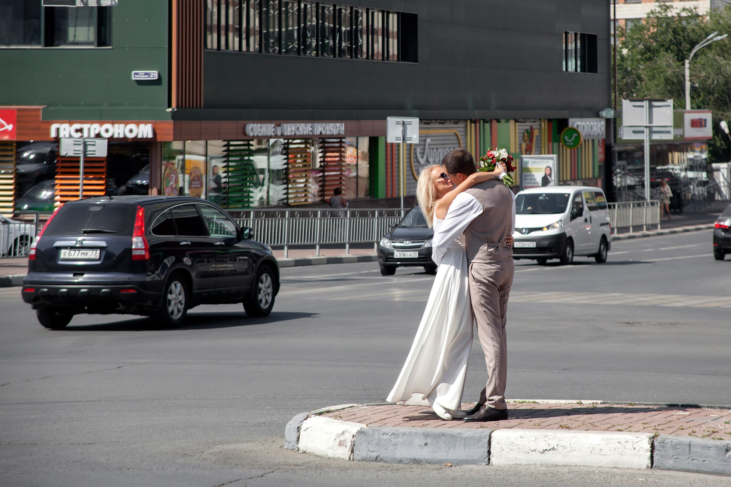 Жених с невестой целуются на перекрестке в городе, мимо проезжают машины - свадебная фотосессия Ульяновск