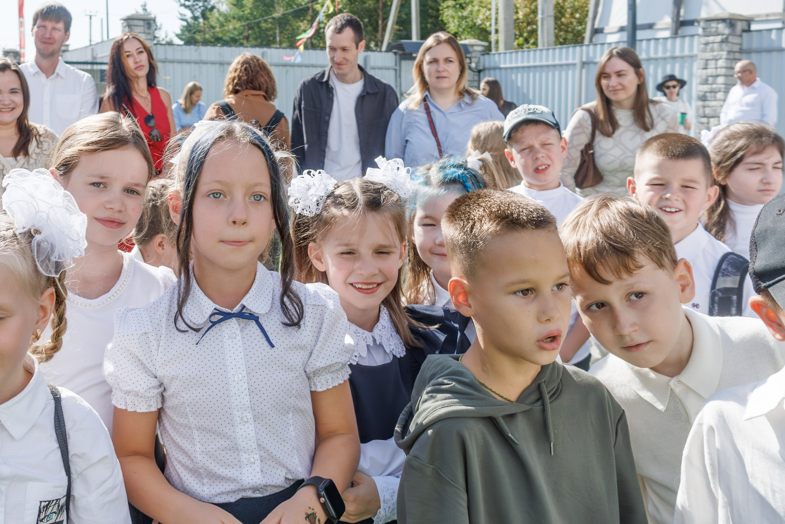 Линейка 1 сентября в школе - дети с букетами, радостные родители и учителя; дети обнимаются, радуются встрече с друзьями после каникул