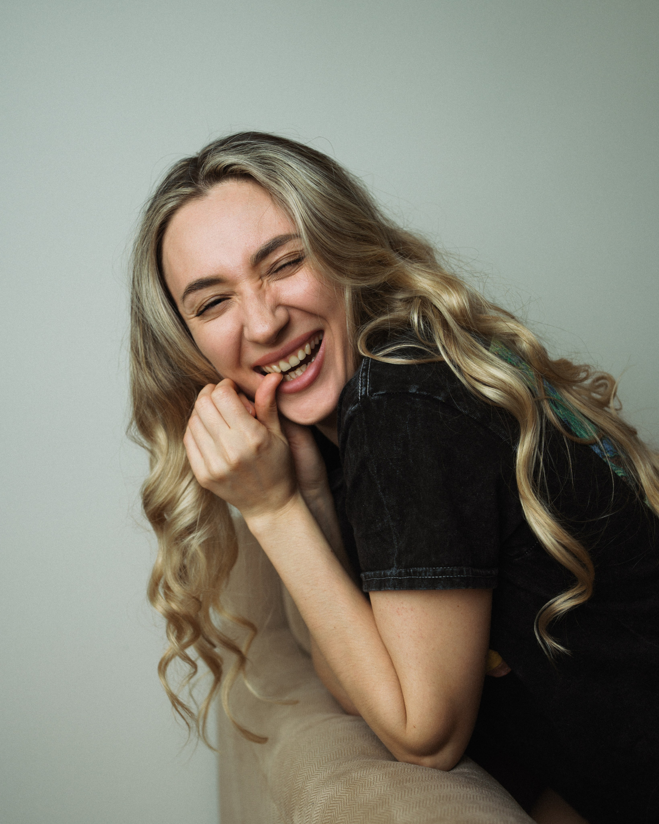 Женщина смеётся, сидя на диване, рука у подбородка — фотограф Виталий Кожевников