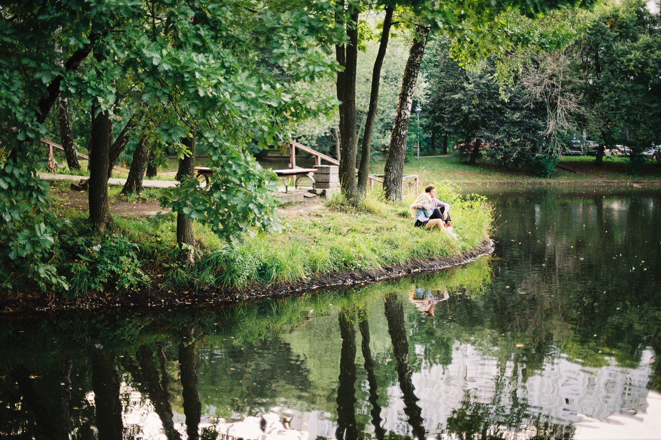 Парень с девушкой сидят в обнимку на берегу пруда летом