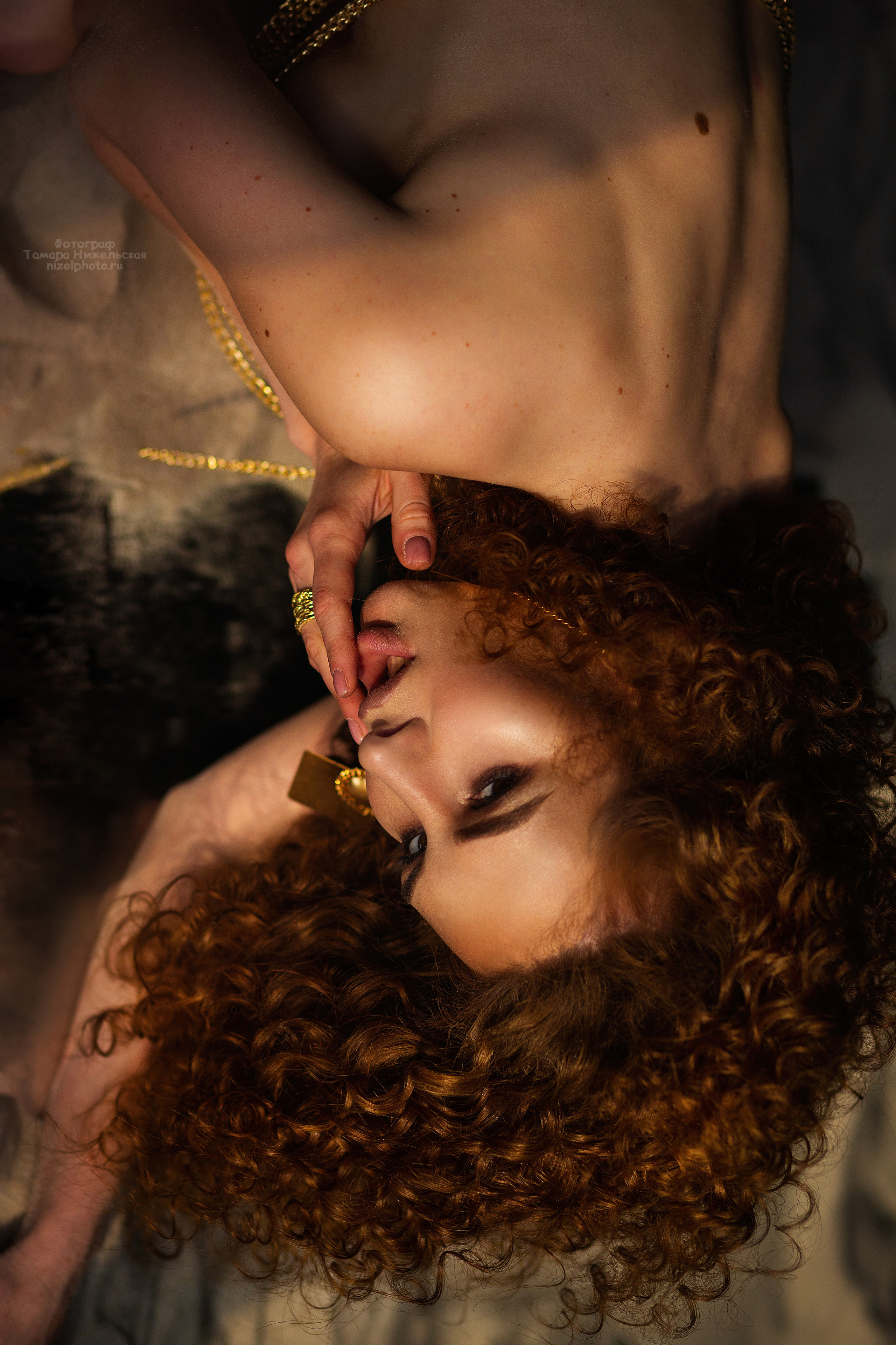 Обнаженная  девушка  с рыжими волосами лежит  на  песке. Рядом  лежит  зеркало.