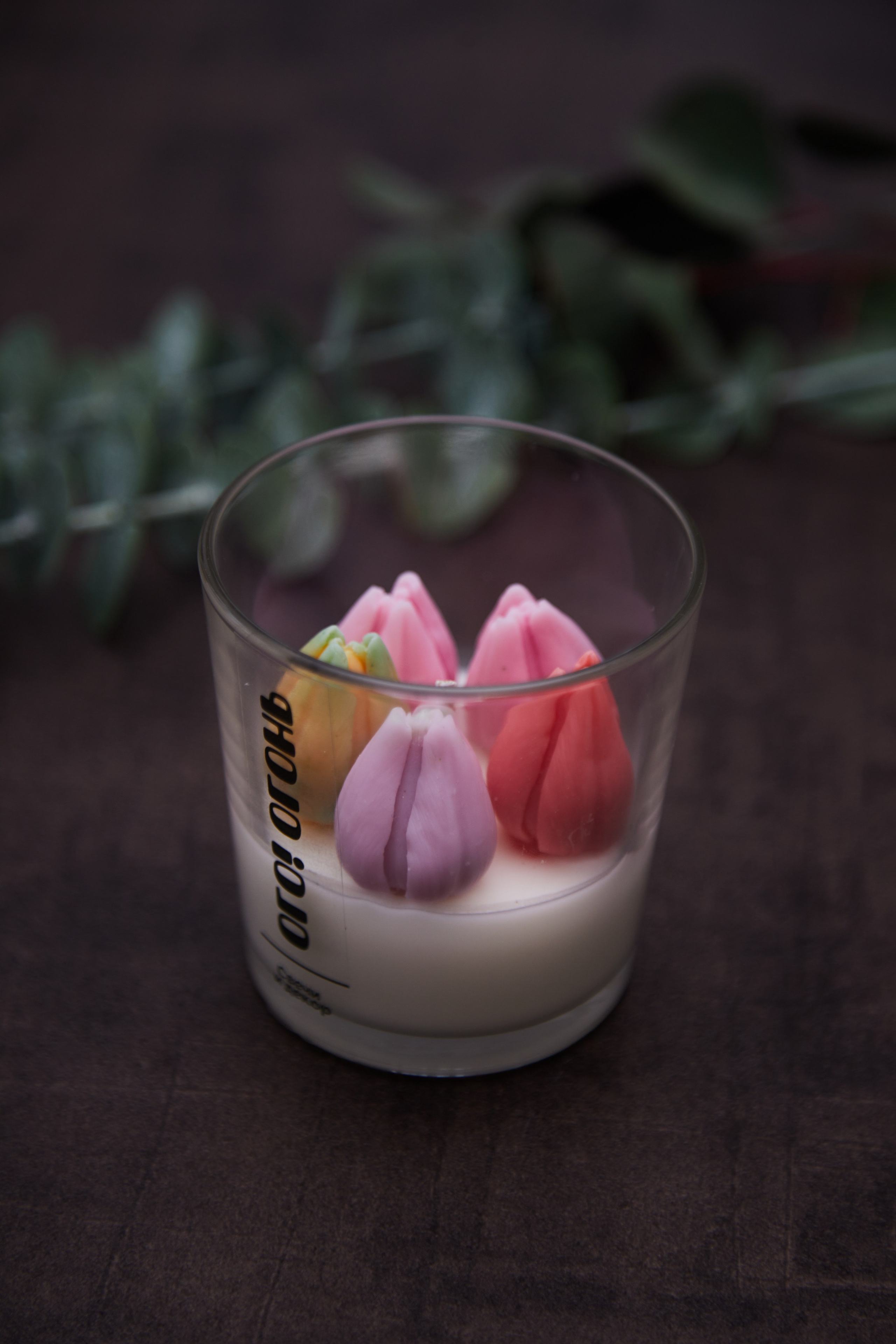 Каталожное фото свечи в стакане с декоративными цветами.