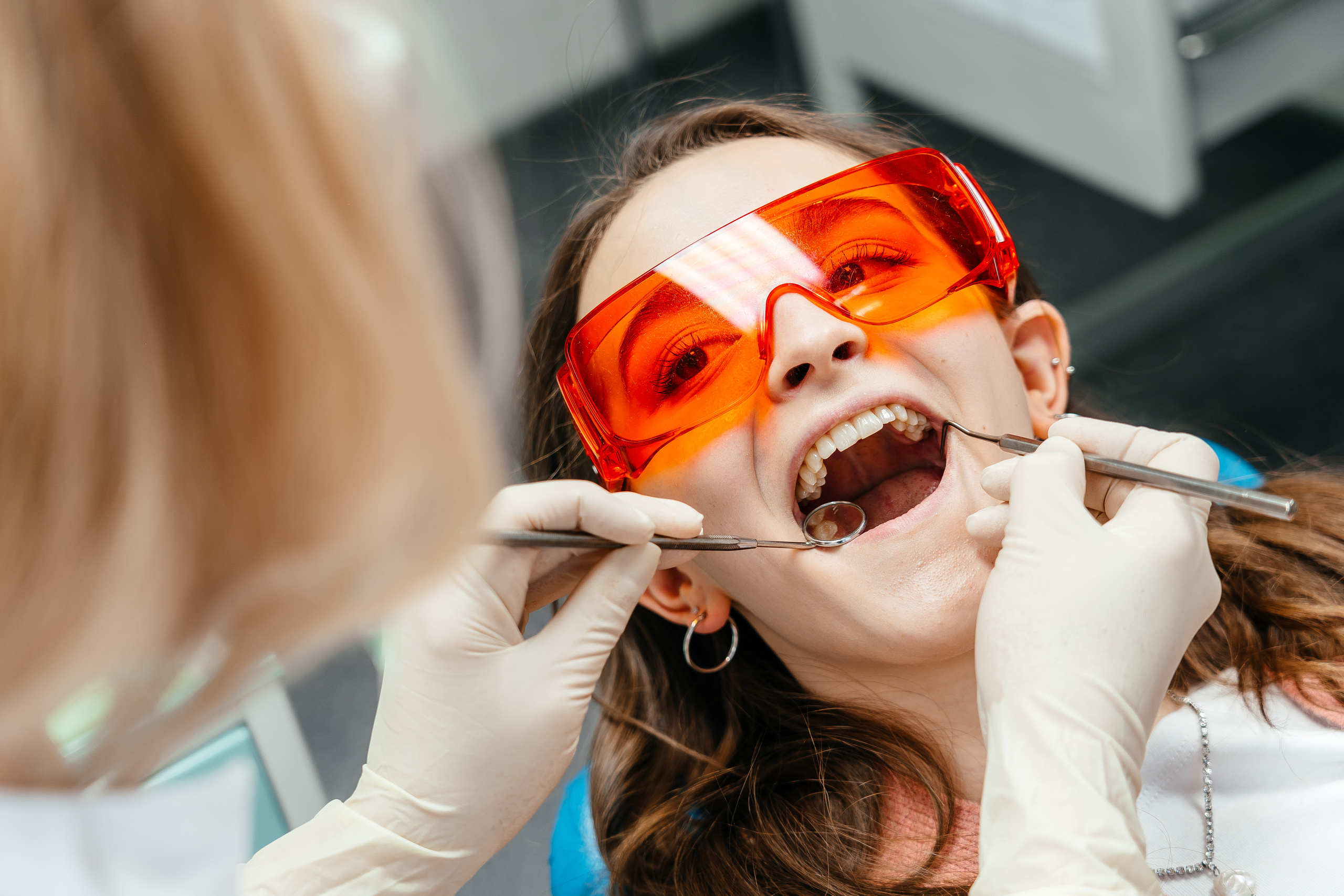 стоматолог проводит осмотр полости рта пациента, девушка на приеме у дантиста