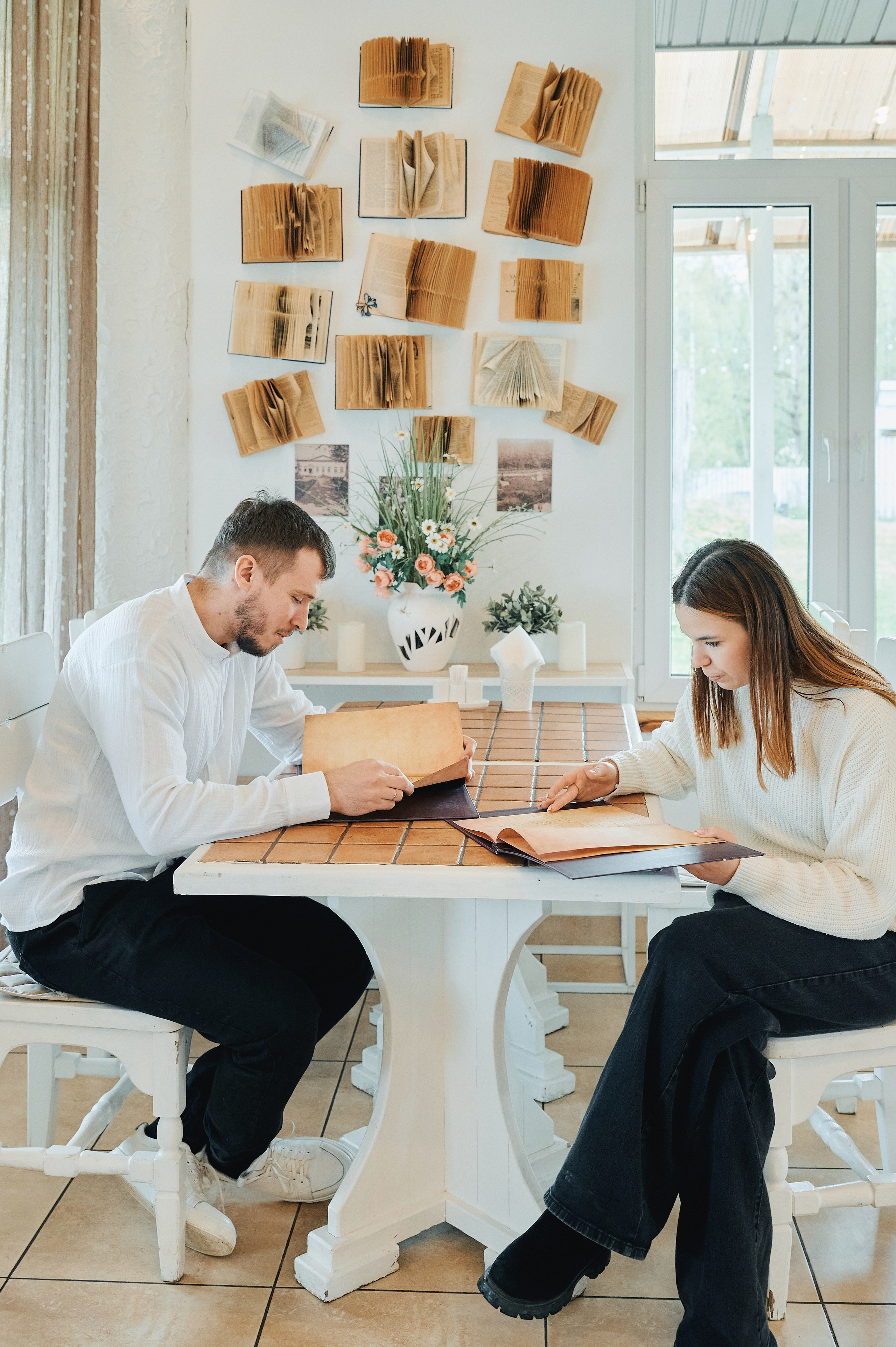 Мужчина и женщина сидят за столом с меню в кафе, на стене позади книги и фотографии
