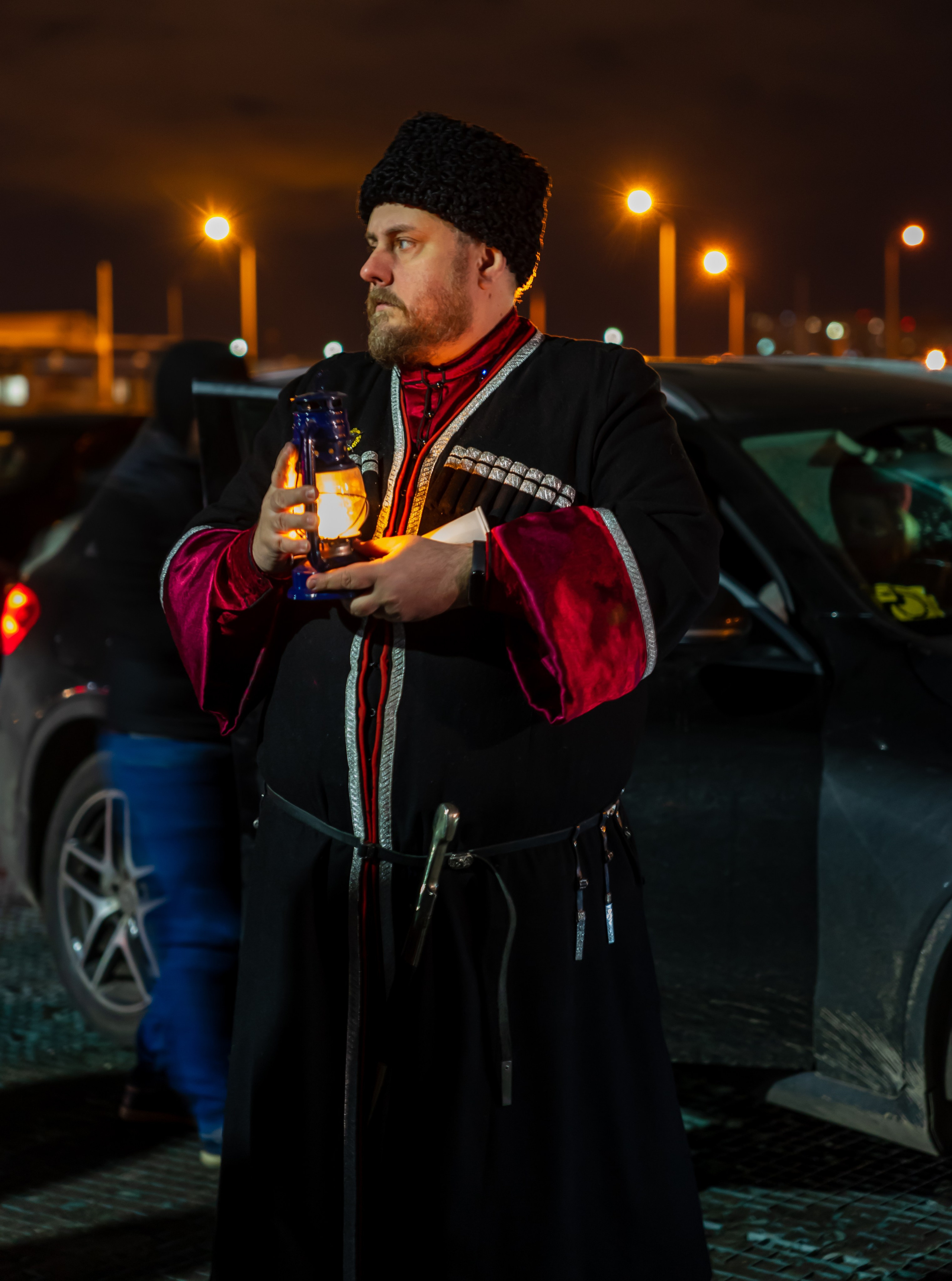 Встреча Благодатного огня Пасха 2022 Пулково: мужчина в традиционном русском костюме с лампадой и фонарём на парковке аэропорта ночью, атмосферный кадр Санкт-Петербург, фото Мальцев Евгений evrednix.ru.