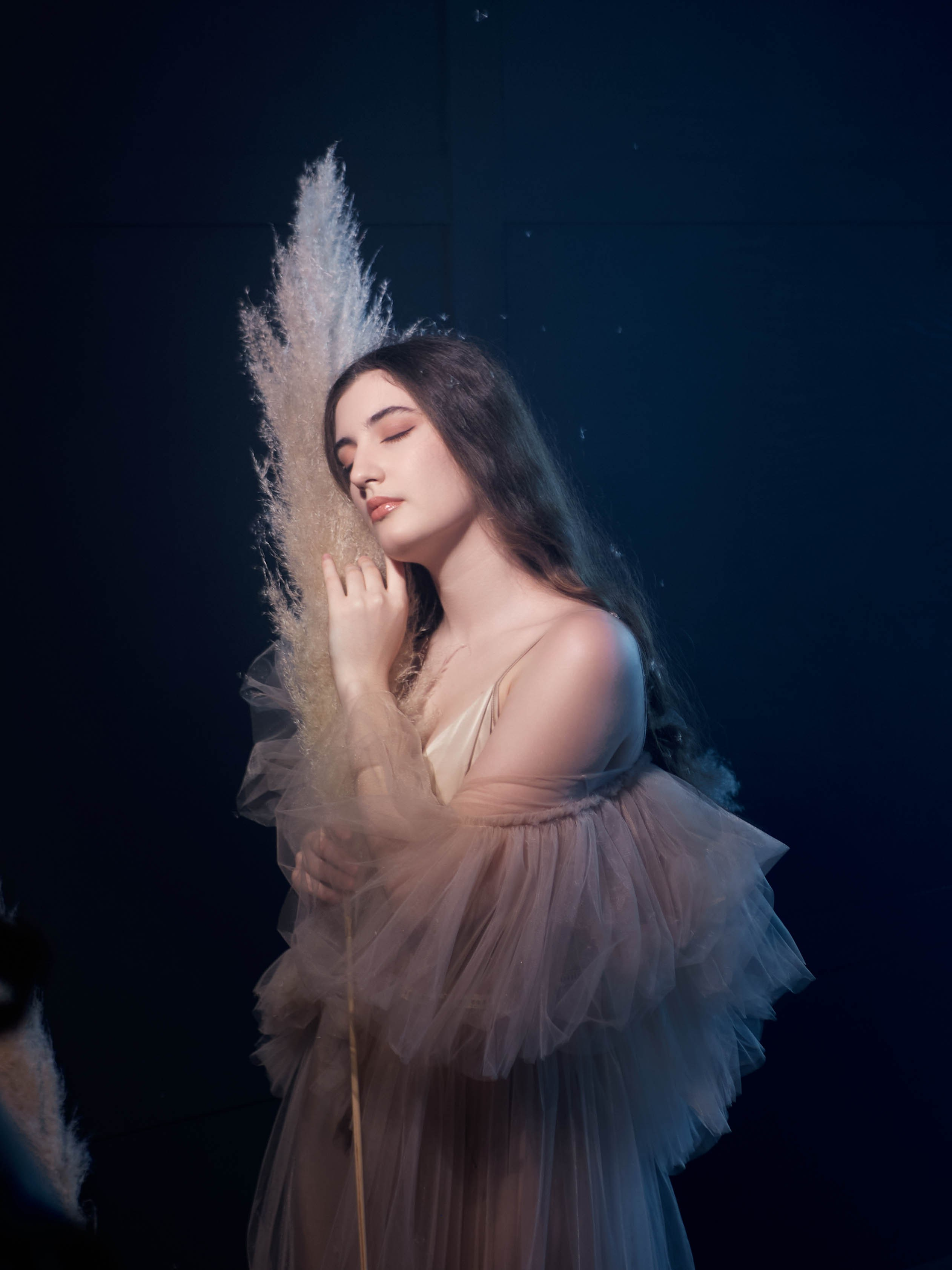 Девушка в бежевом платье на тёмном фоне, её освещает тёплый постоянный источник света.