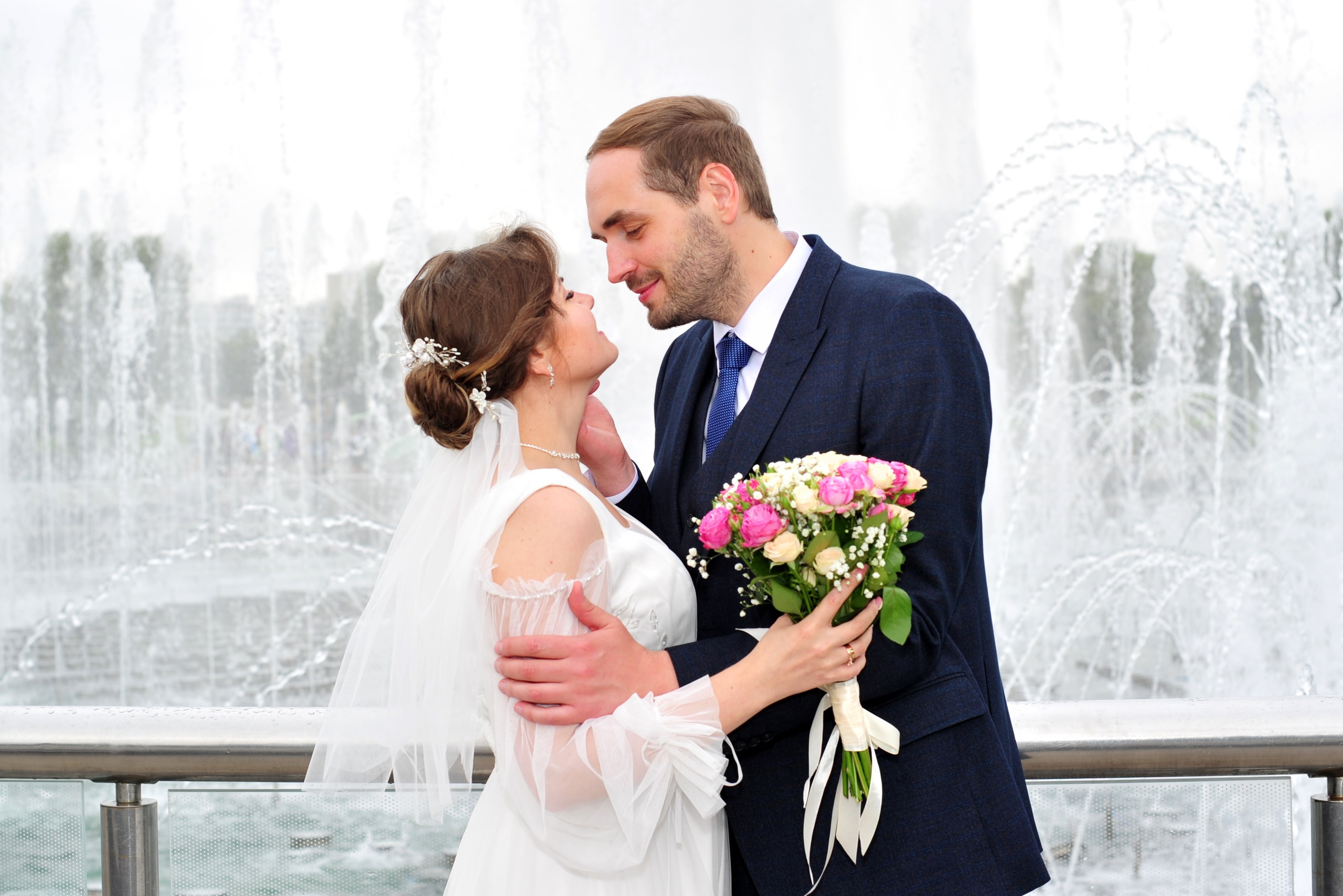 Свадьба в Царицыно пасмурным летним днем, молодожены смотрят друг на друга на фоне фонтанов и струй воды