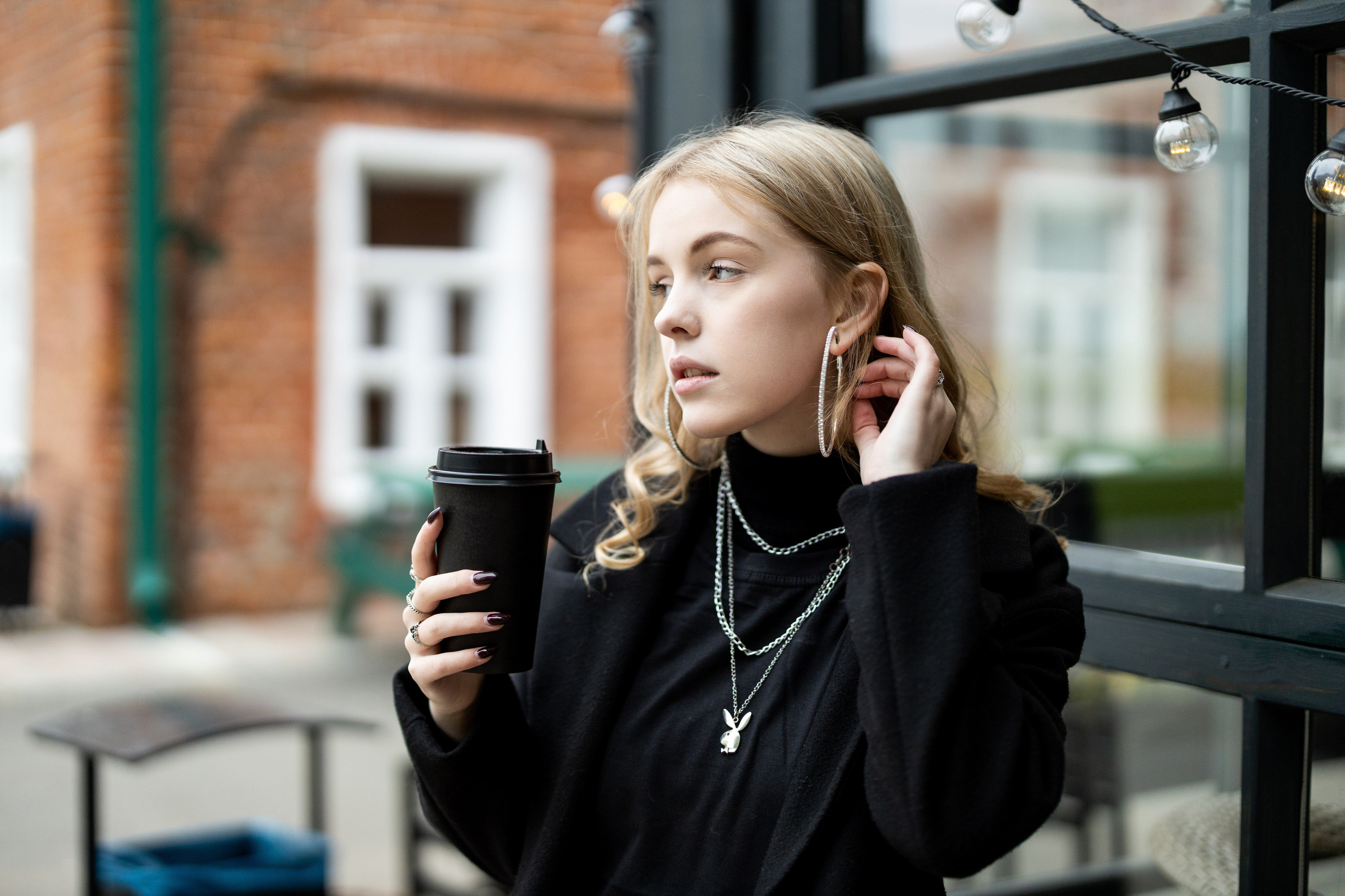 Коломчанка в чёрном со стаканчиком кофе в руке смотрит вдаль.
