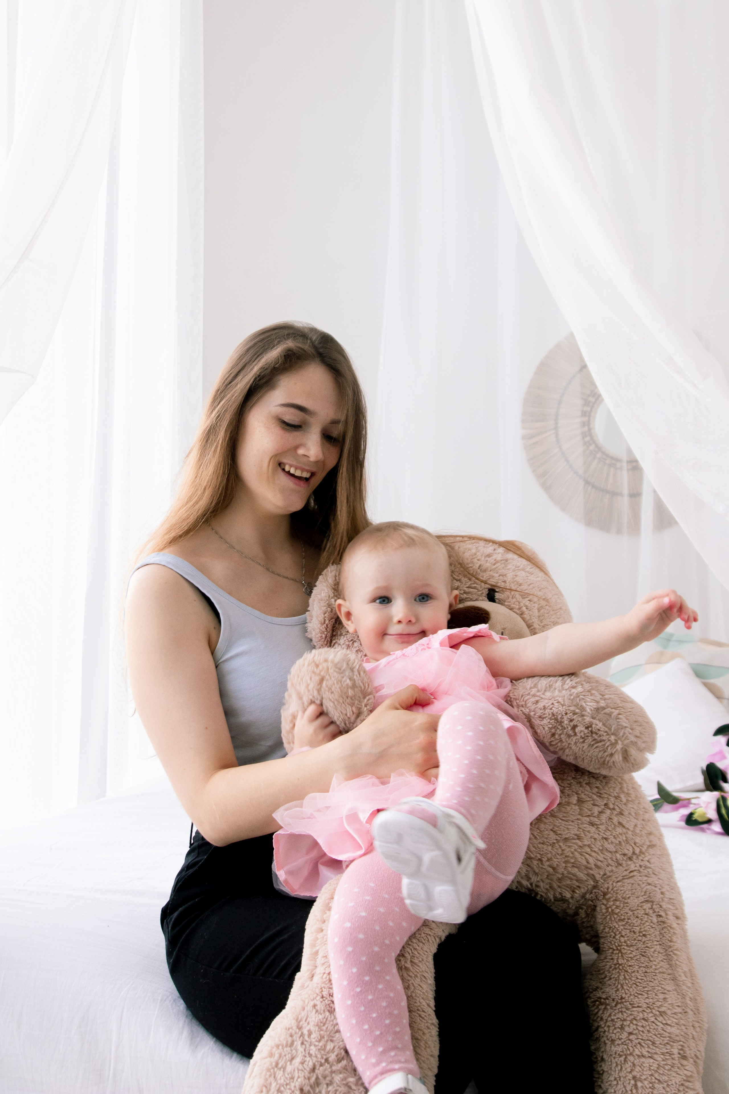 мама сидит на кровати и пытается удержать свою маленькую любопытную дочку