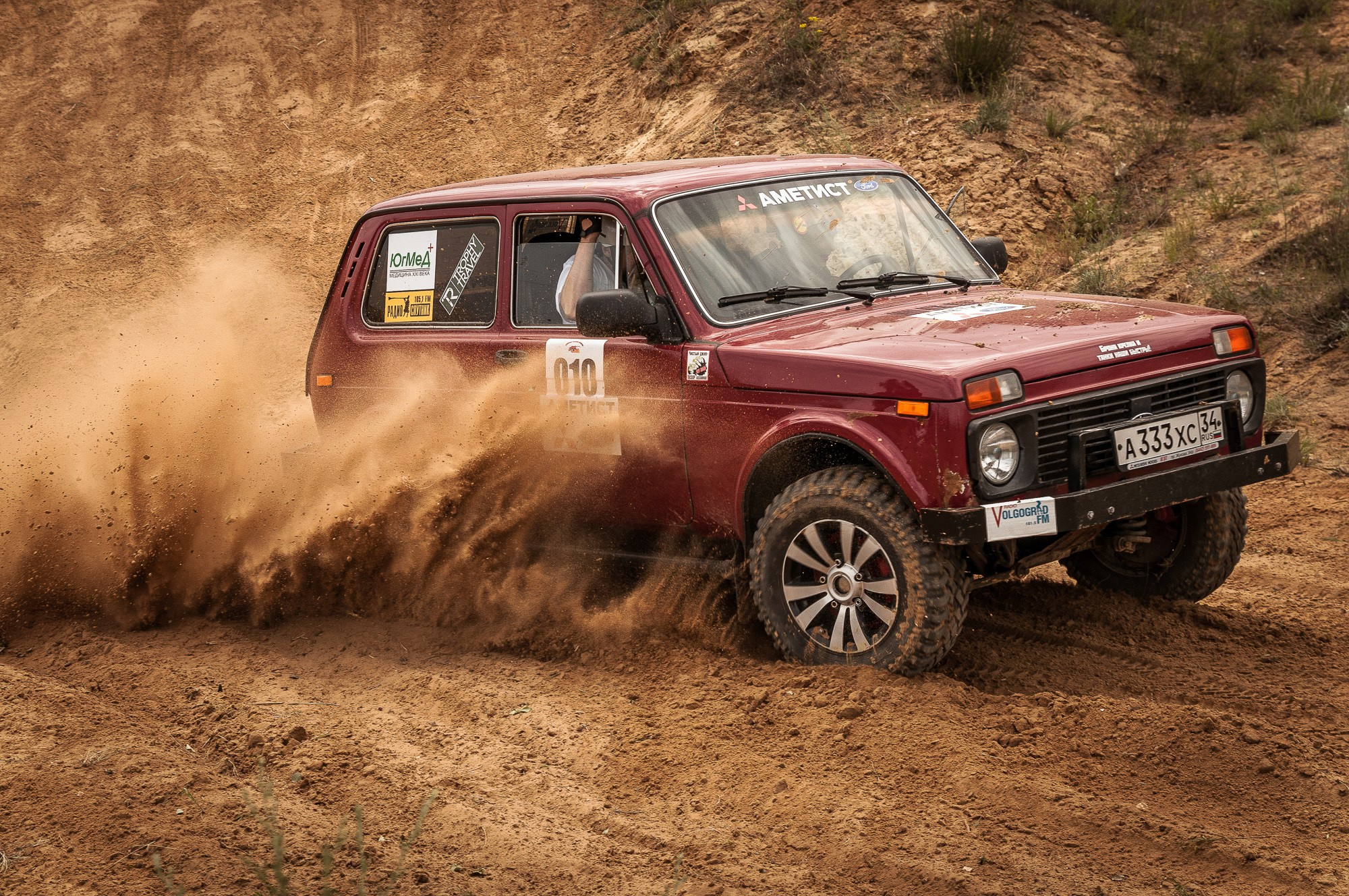 Красная Нива на гоночной трассе, из-под колёс которой вылетает облако пыли