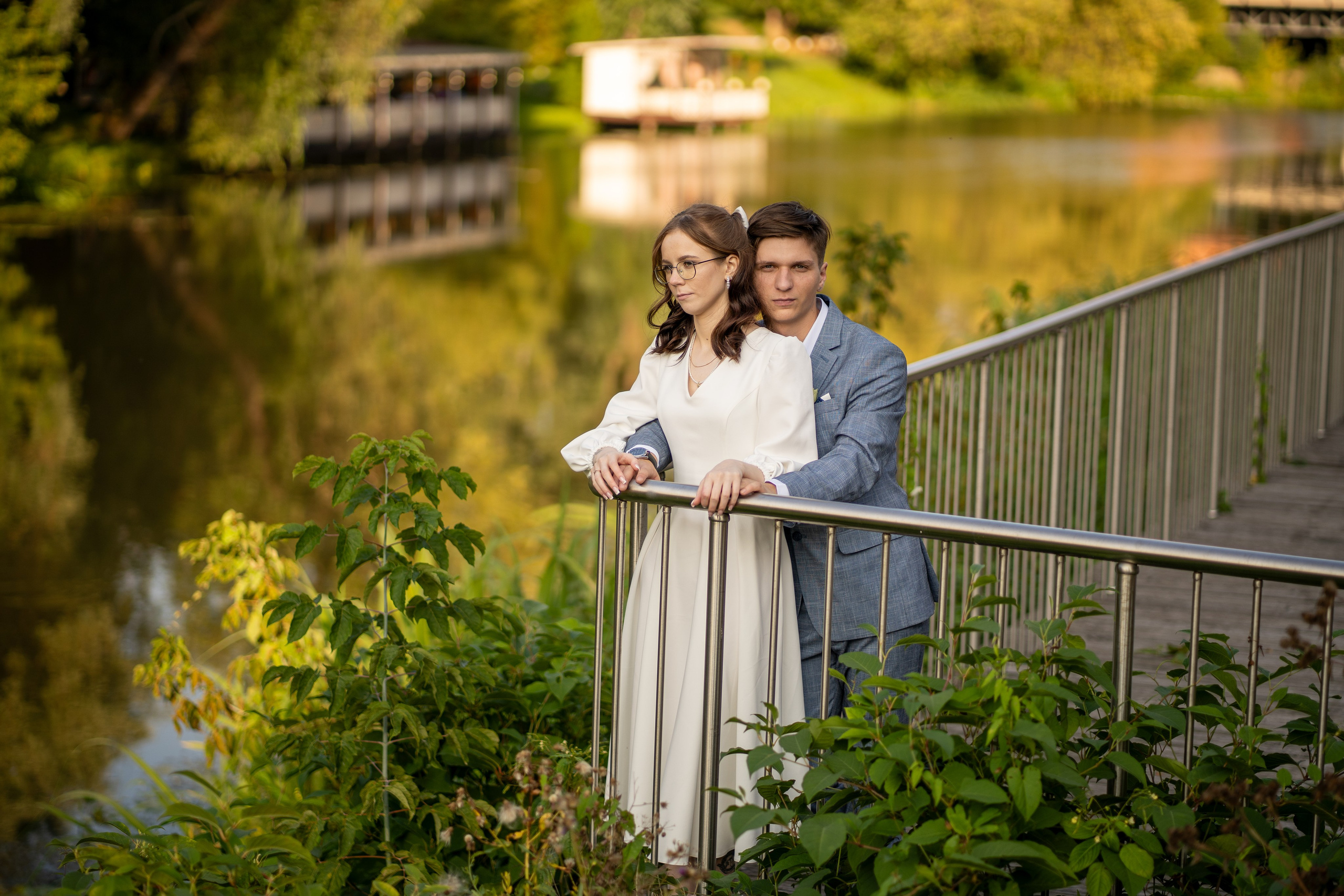 Молодожены обнимаются на мосту у реки