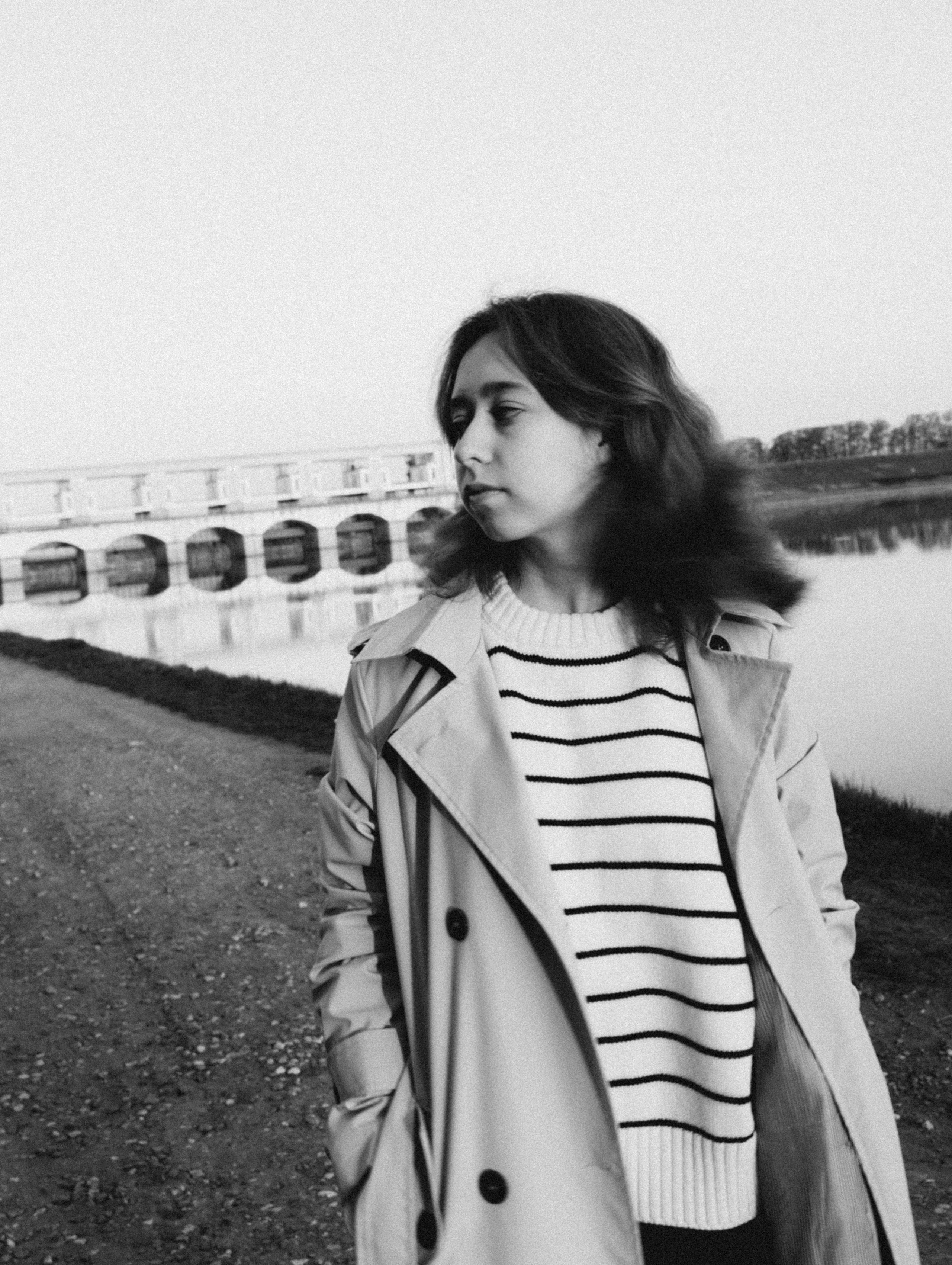 Черно-белая фотография девушки в полосатом свитере на фоне реки.