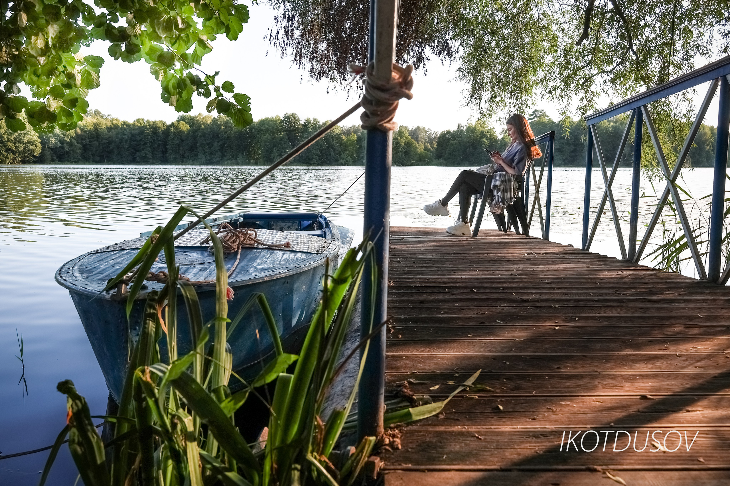 Фотограф Илнар Котдусов - портрет сидящей девушки на причале с лодкой у озера.