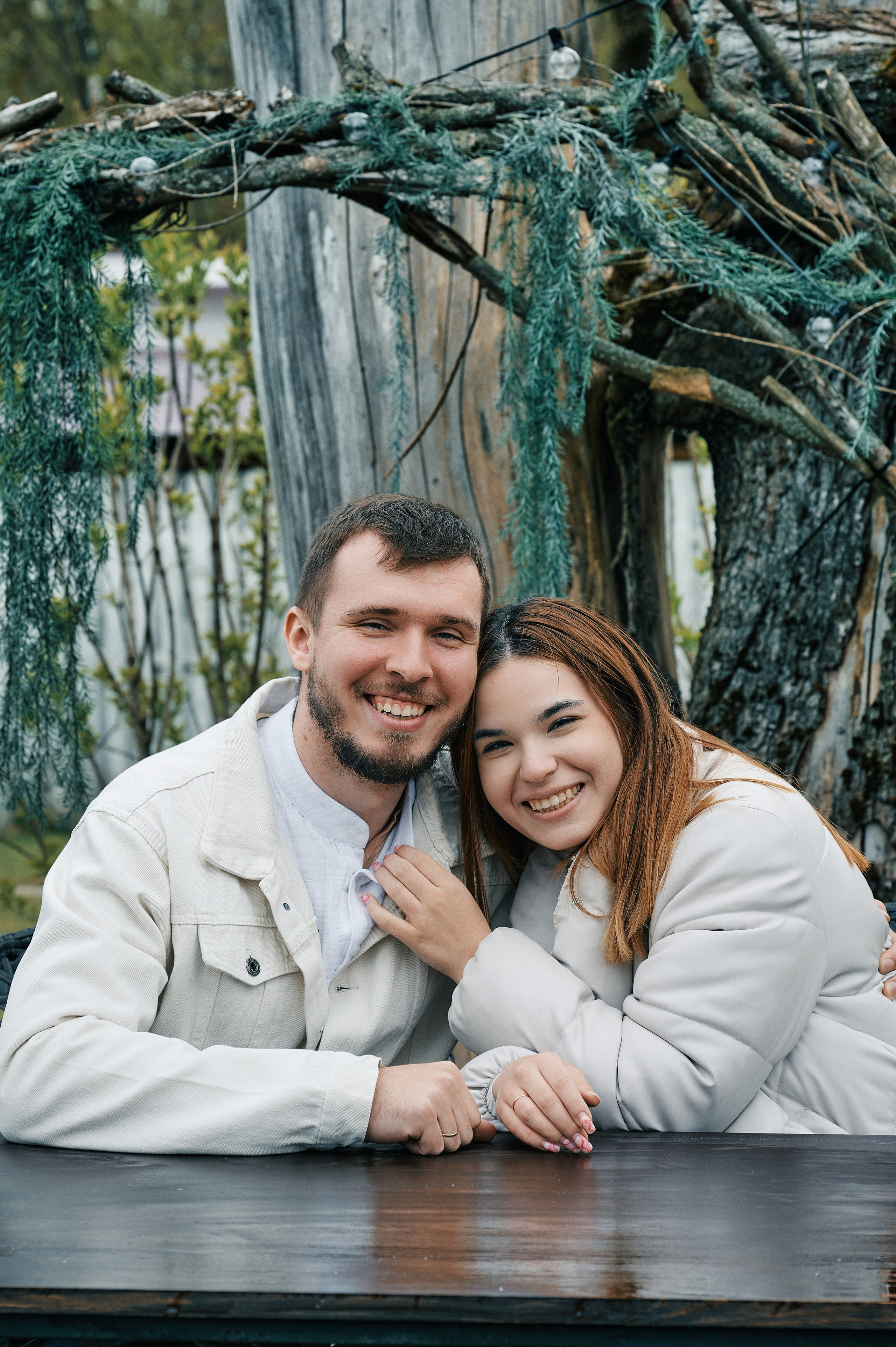 Молодая пара улыбается, сидя за деревянным столом на улице