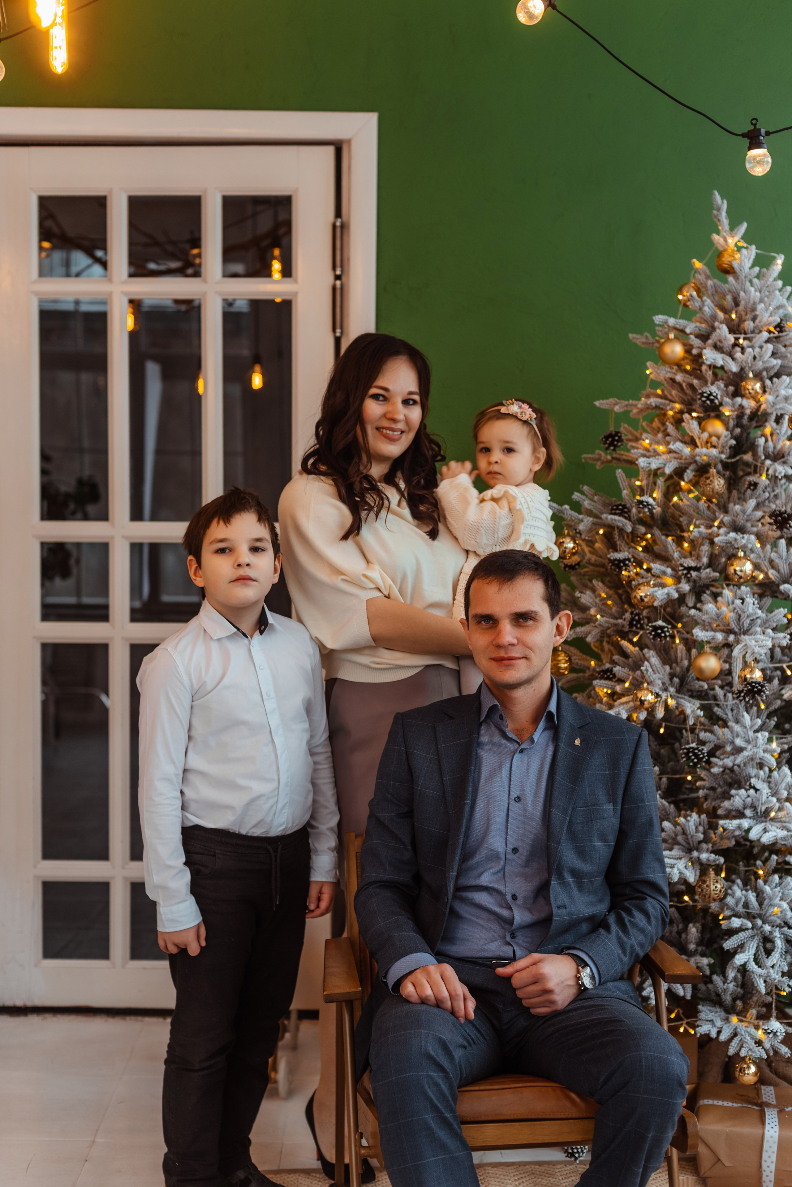 Новогодняя фотосессия семьи из четырех человек: мама, папа, старший сын и маленькая дочка позируют на фоне украшенной елки.