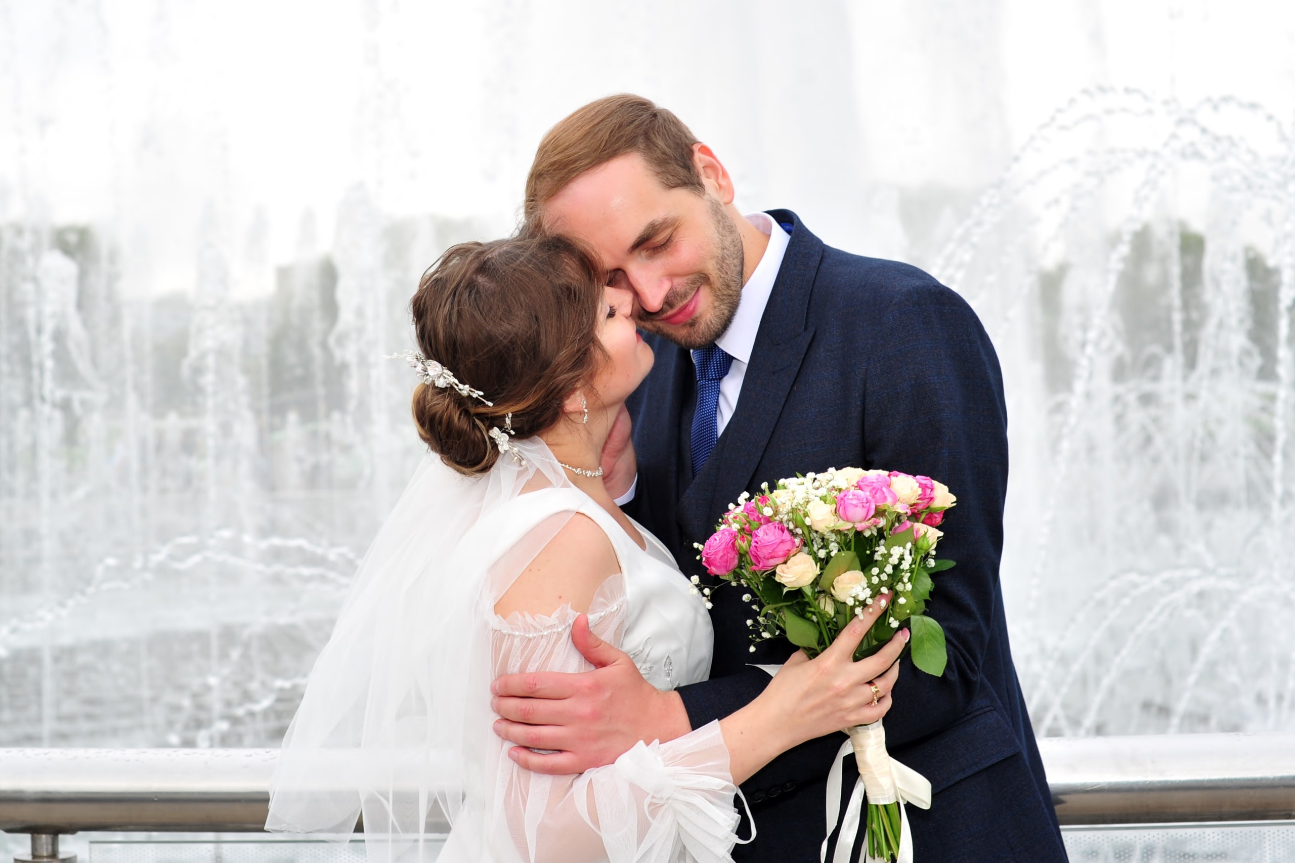 Свадьба в Царицыно пасмурным летним днем, поцелуй новобрачных на фоне фонтана и струй воды 