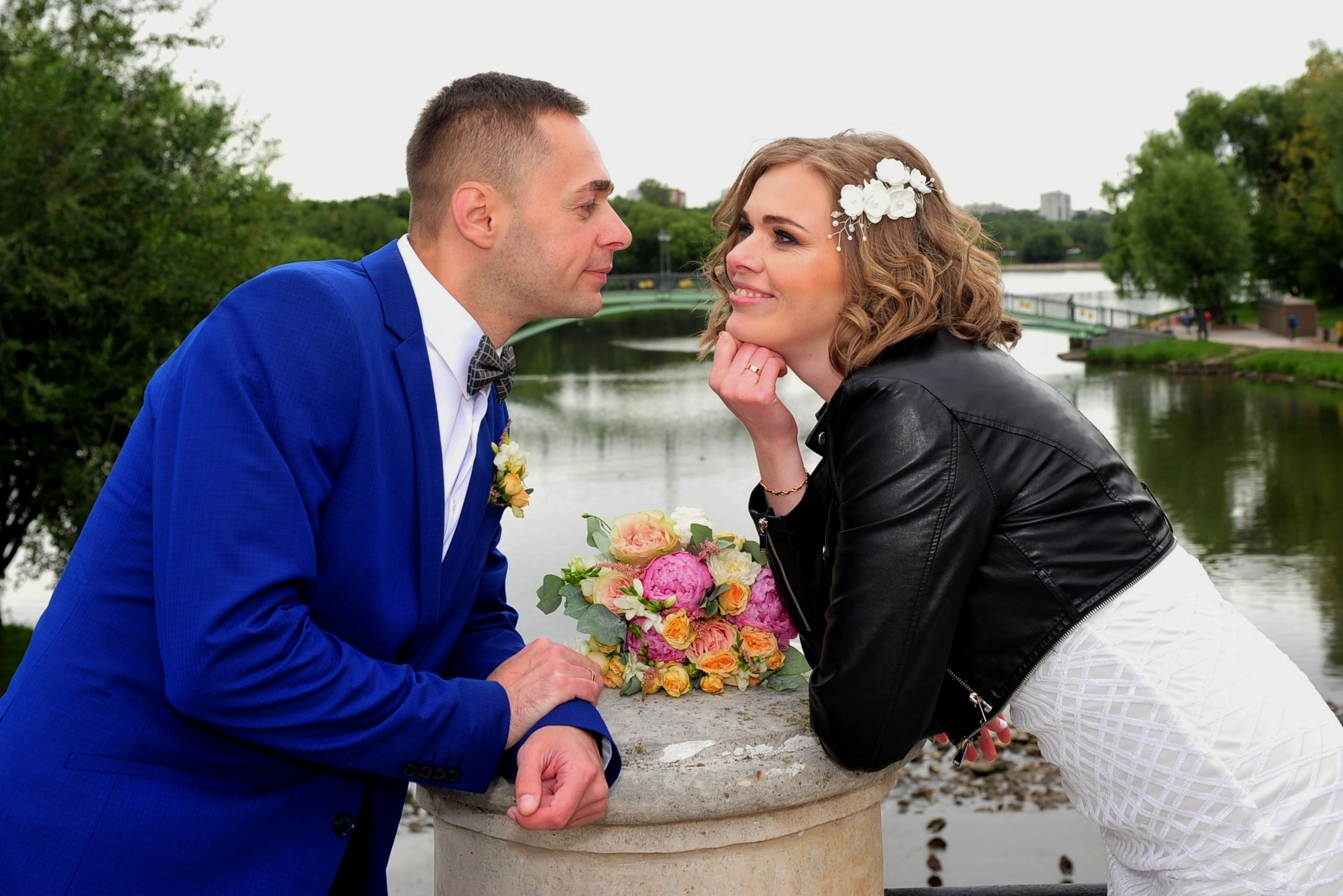 Свадьба в Царицыно хмурым прохладным летним днём, жених и невеста стоят на белокаменном мосту на фоне пруда и смотрят друг на друга, между новобрачными лежит букет невесты