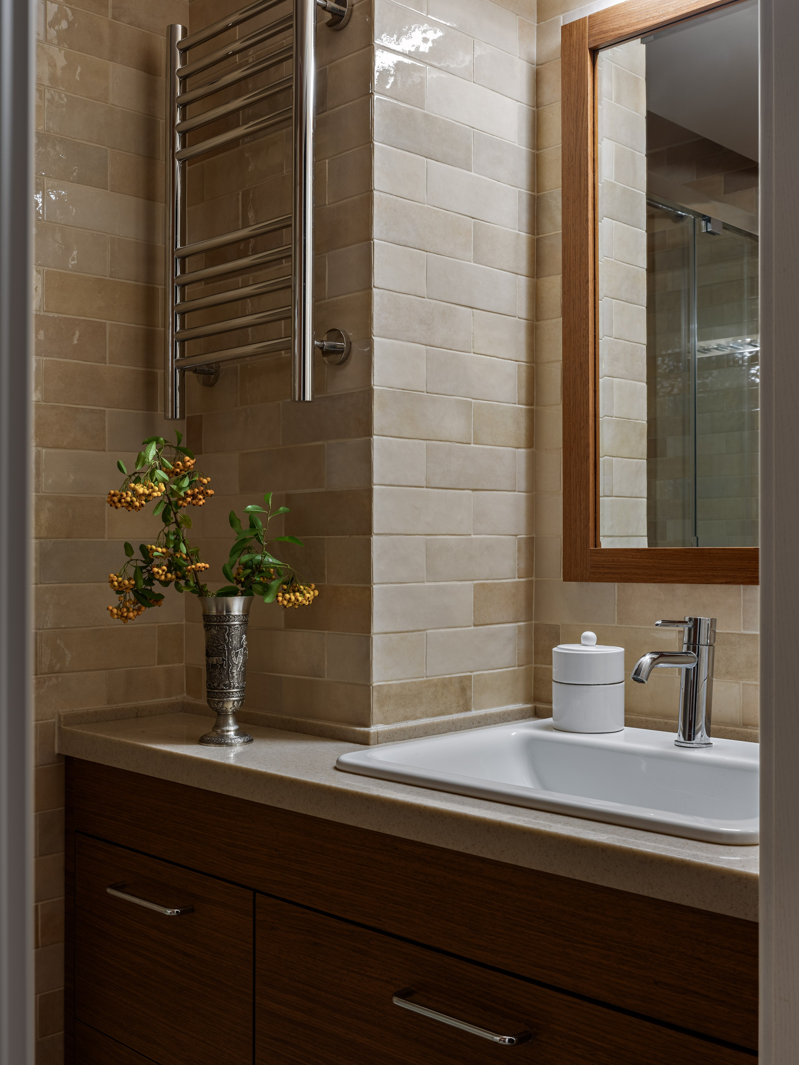 Санузел с умывальником, деревянной тумбой, зеркалом в раме и металлическим полотенцесушителем на фоне бежевой плитки, дополненный вазой с декоративными ветками; дизайн Юлии Капункиной и Альбины Терещенко, стилистика Алины Нелень, фото Сергея Денисенко.