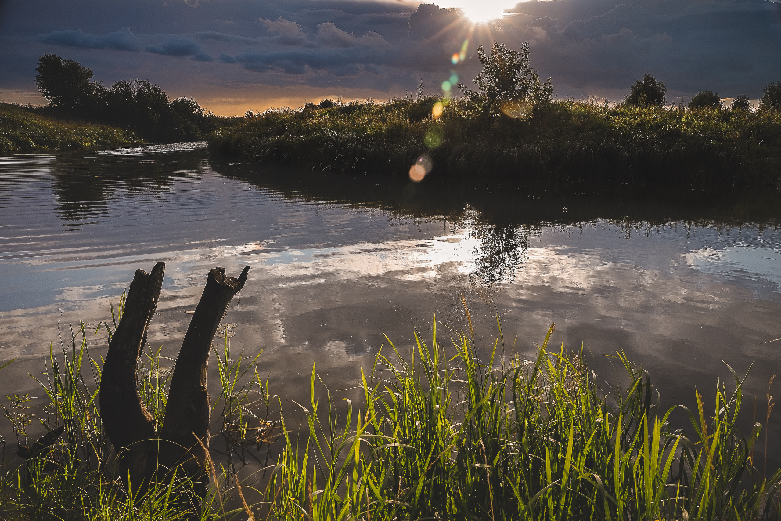 Солнце пробивается через дождевую тучу летним вечером на реке