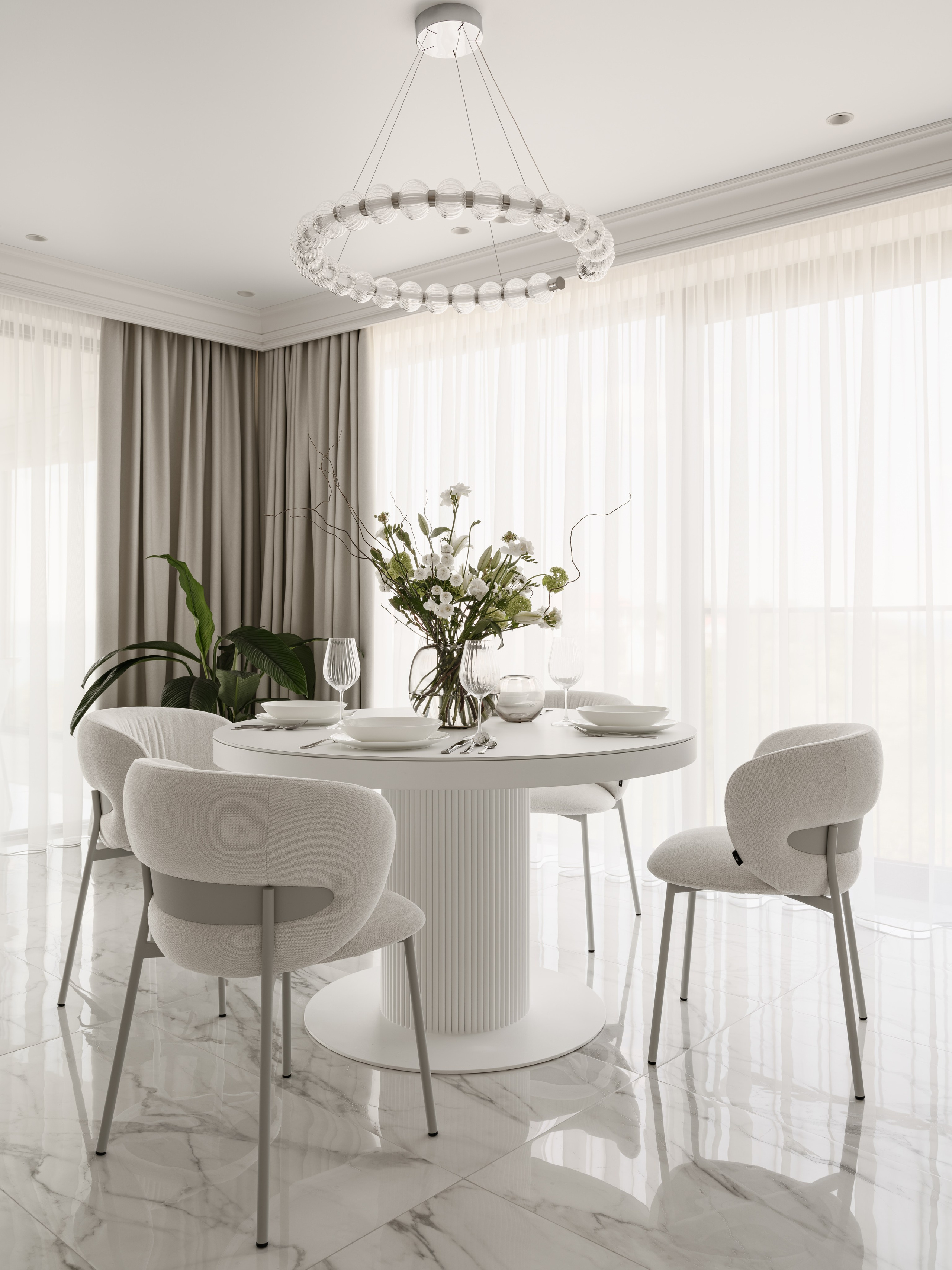 Уютная обеденная зона у панорамных окон с лёгкими шторами, круглым столом и современными стульями, свежие цветы в стеклянной вазе создают атмосферу гармонии — оформление интерьера от Алёны Боярской, стилист Наталья Якушева, фотограф Сергей Денисенко.