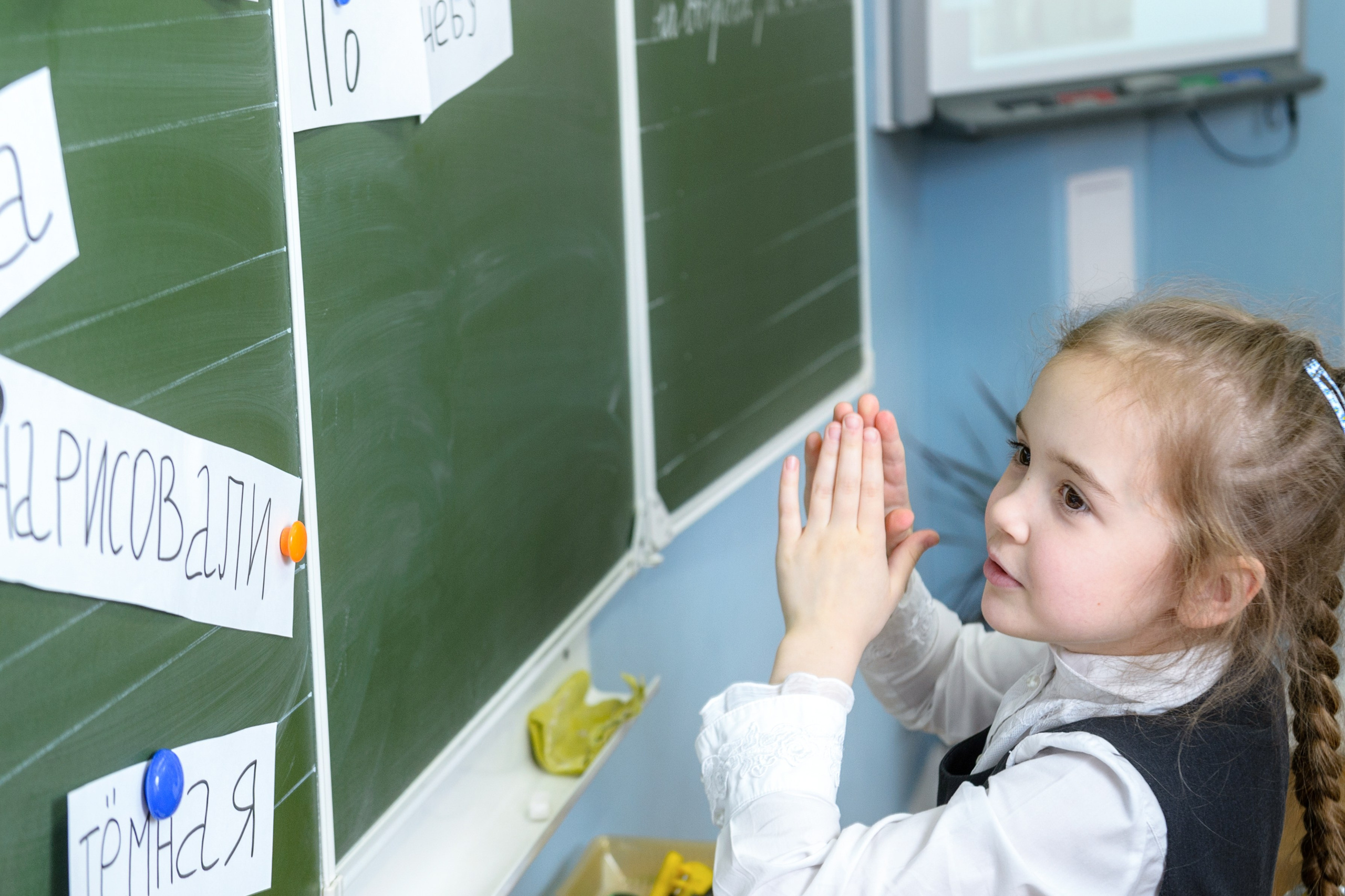 Школьница у доски смотрит на карточки с буквами