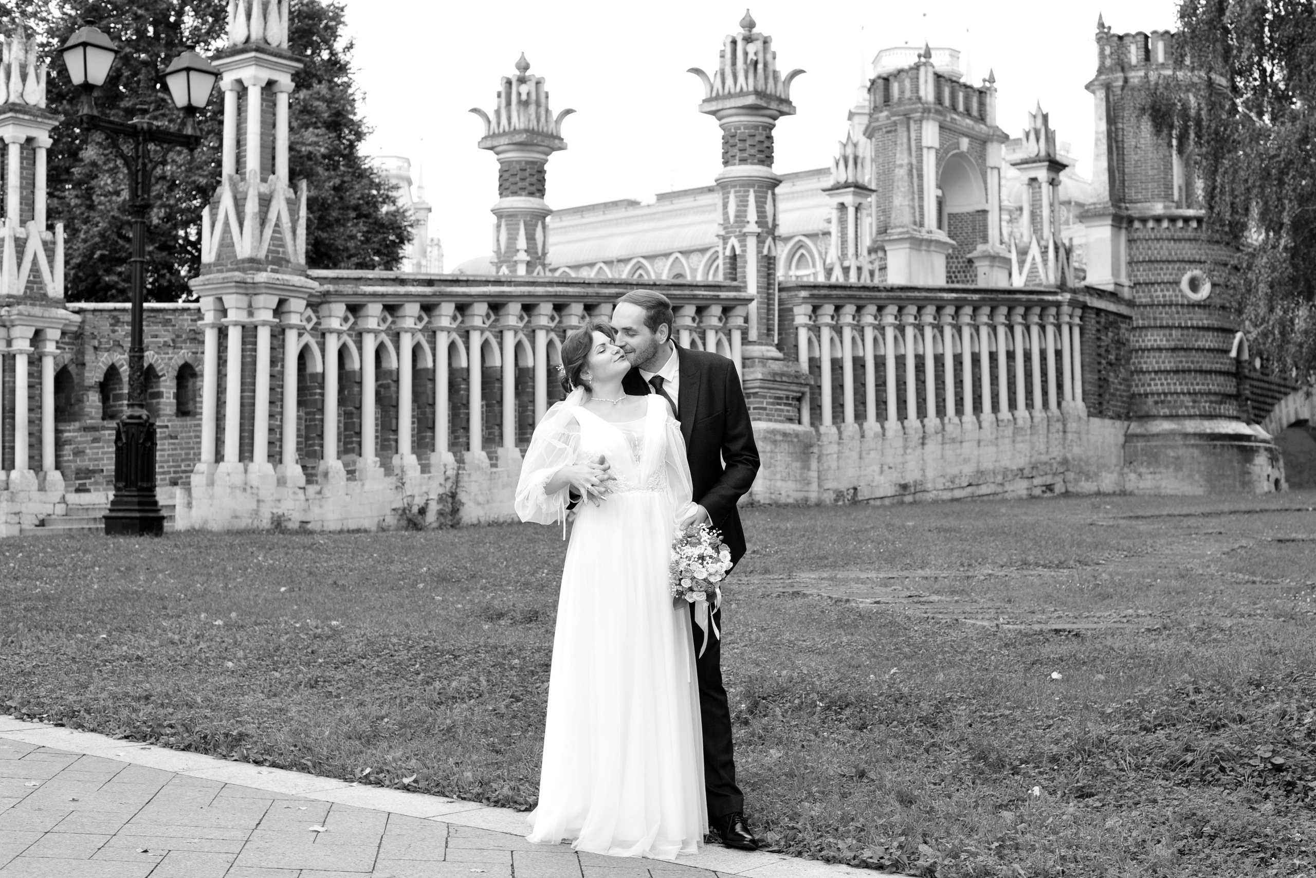 Свадьба в Царицыно пасмурным летним днем, жених и невеста целуются на фоне каменного моста, черно-белая фотография