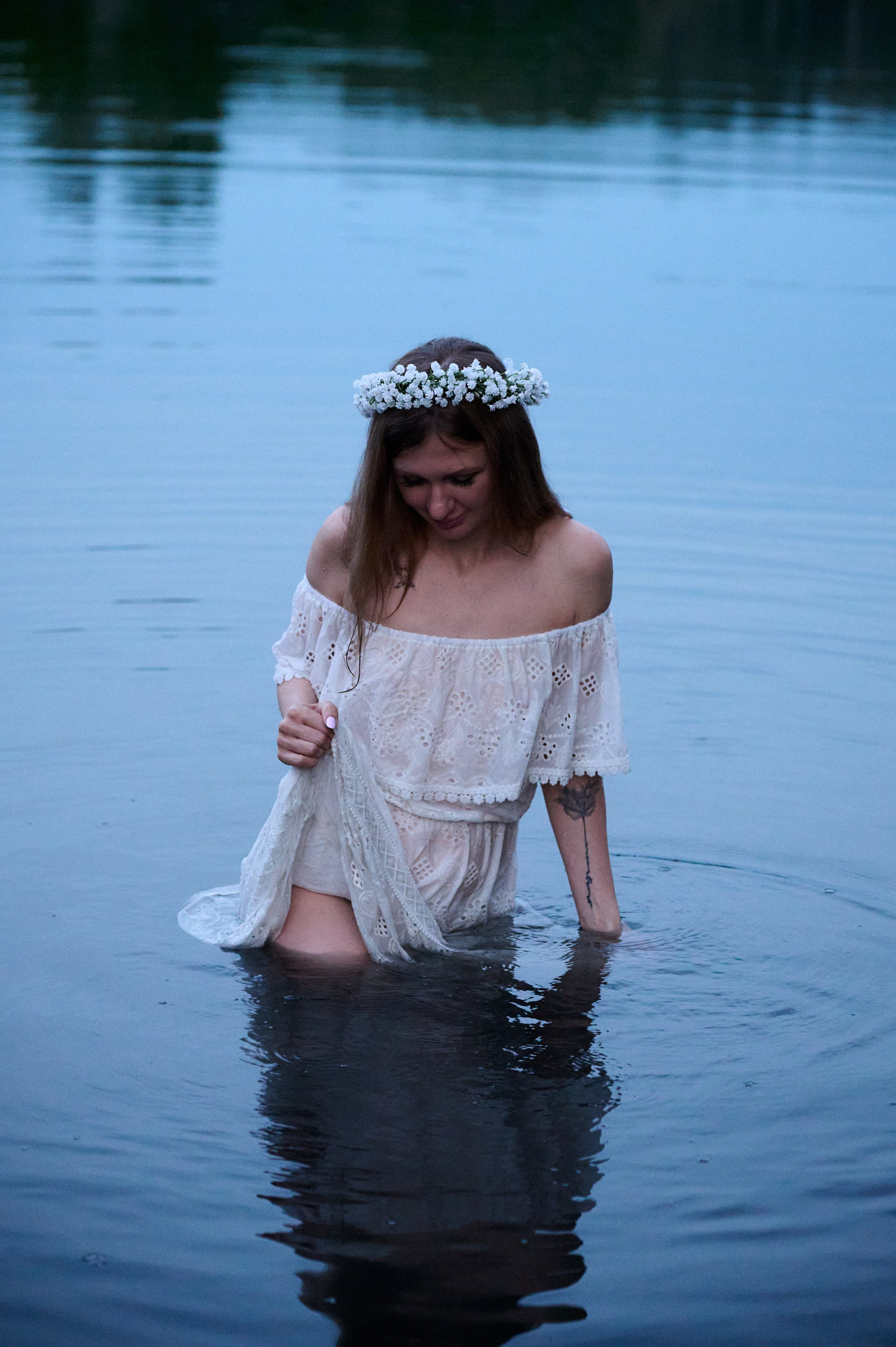Евгения в белом платье стоит по пояс в воде, опустив взгляд.