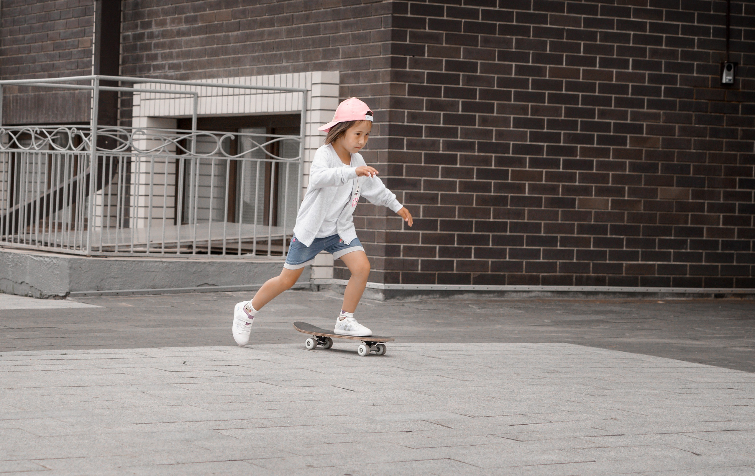 Детская фотосессия летом - девочка стоя в бейсболке едет на скейте