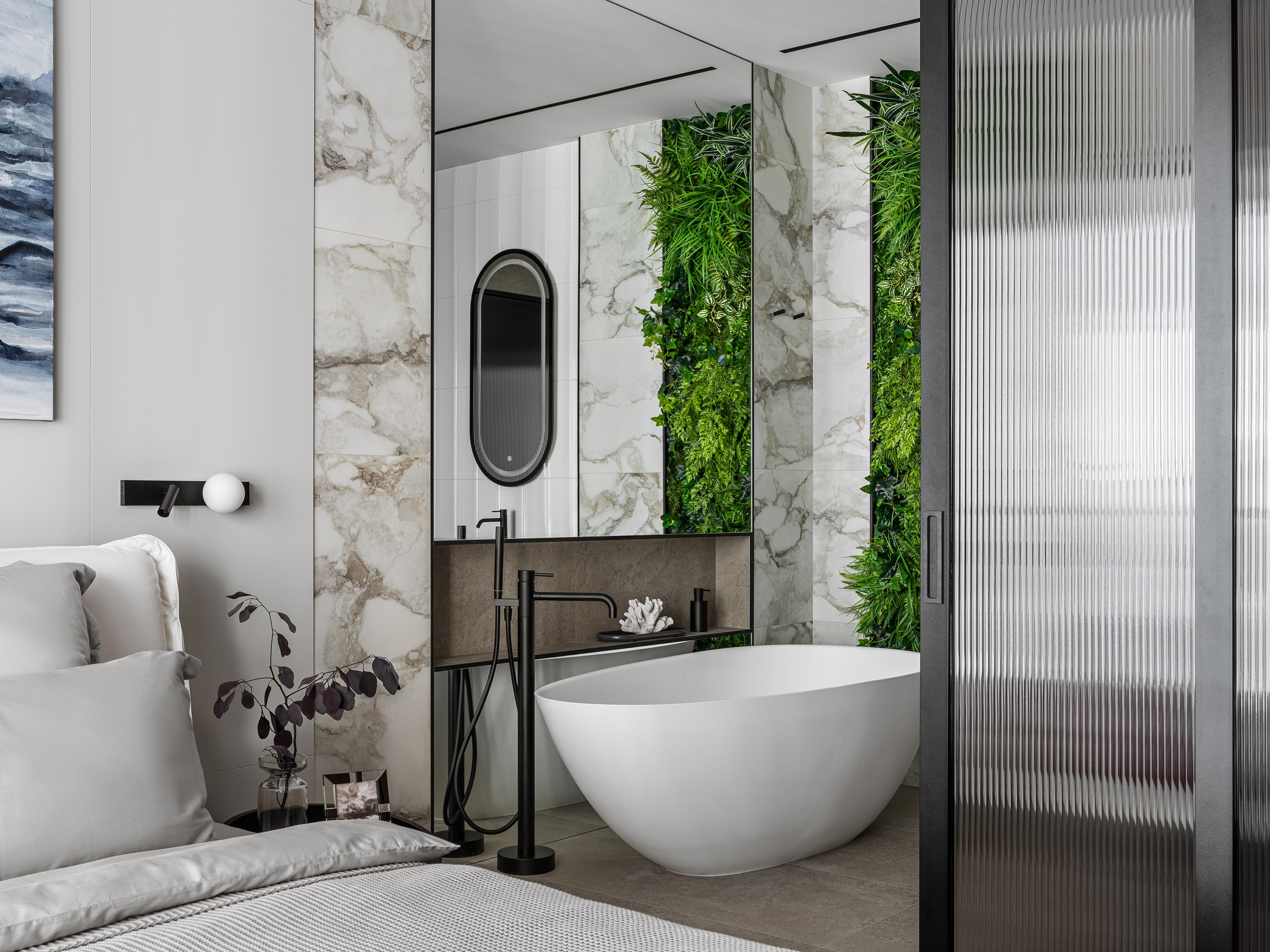 Интерьер спальни, объединенной с ванной зоной: отдельностоящая белая ванна на фоне мраморных панелей и вертикальной фитостены, мягкая кровать с текстилем серого оттенка. Дизайнеры Ренат Байчуков и Алеся Кириенко, стилист Екатерина Ракитина, фото Сергей Денисенко.