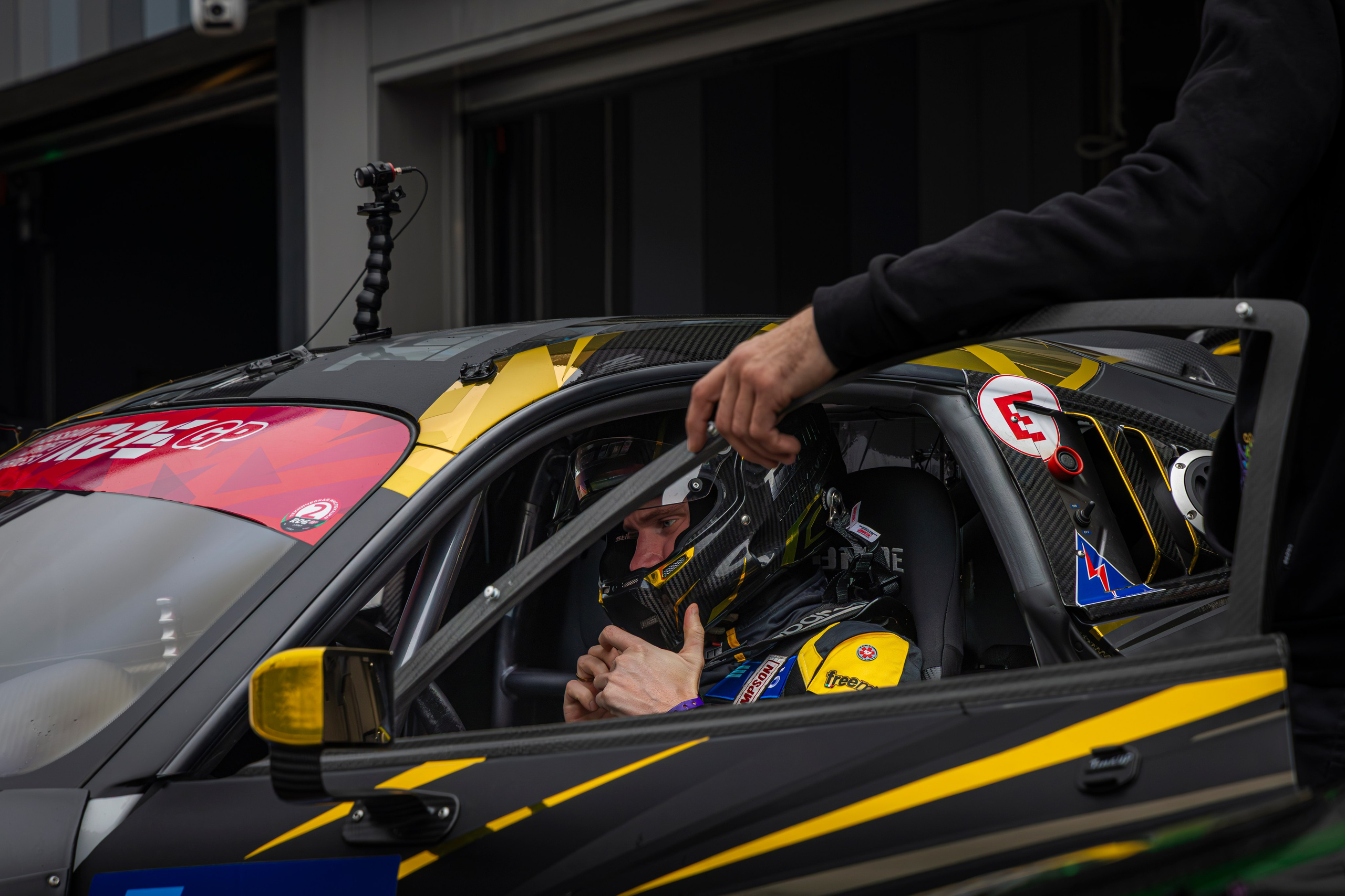 Пилот в гоночном костюме у машины перед стартом — напряжение в глазах