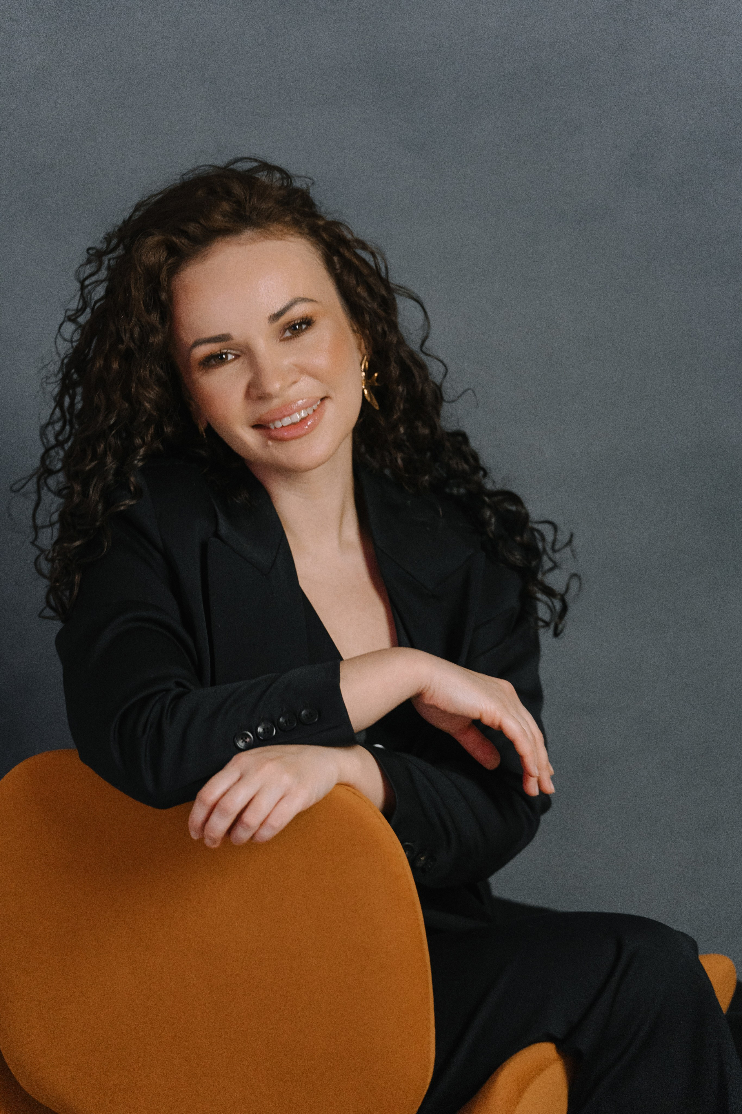 Модель в черном костюме сидит на стуле, создавая неформальный деловой образ в Анапе