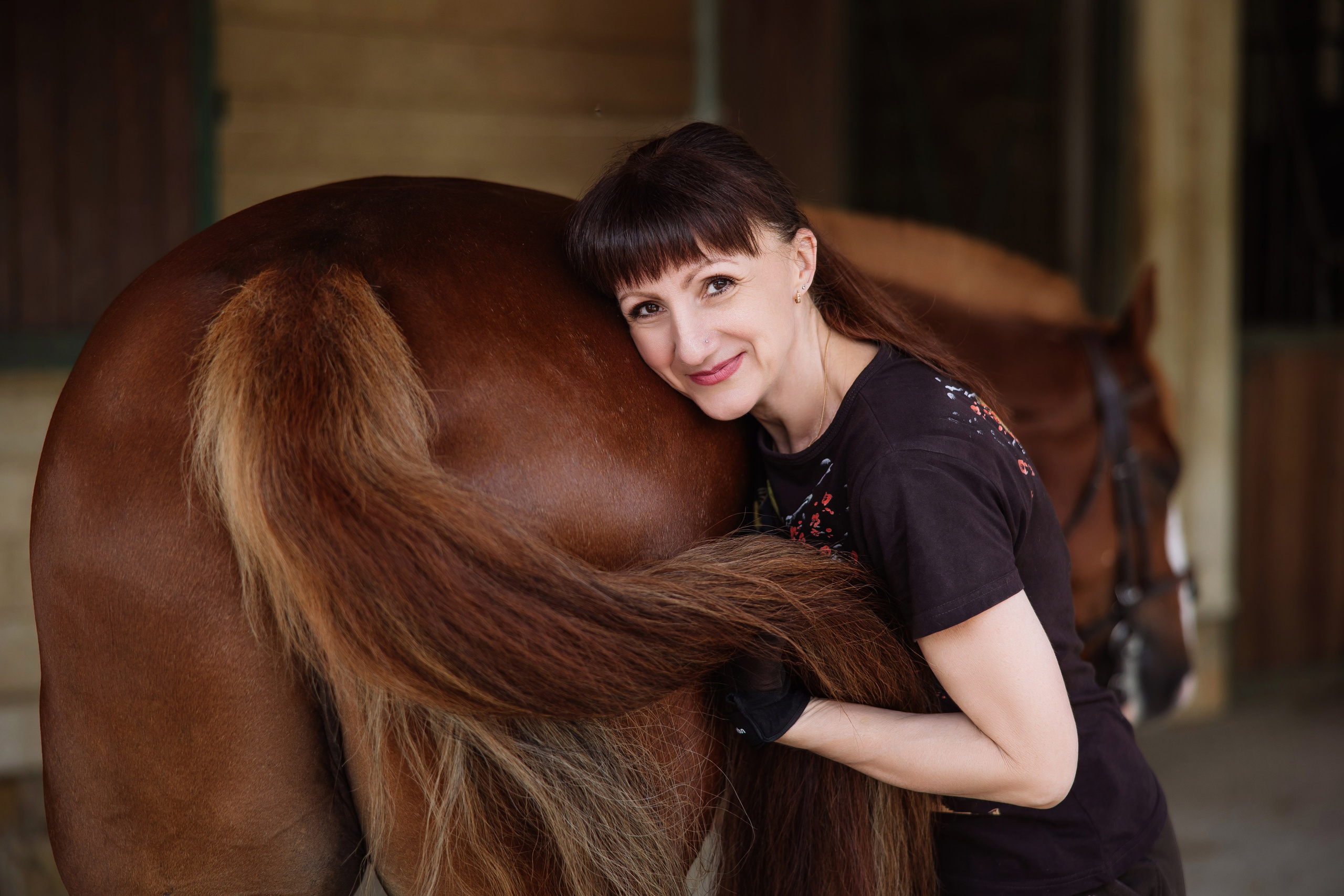 Женский портрет в конюшне - девушка держит хвост лошади