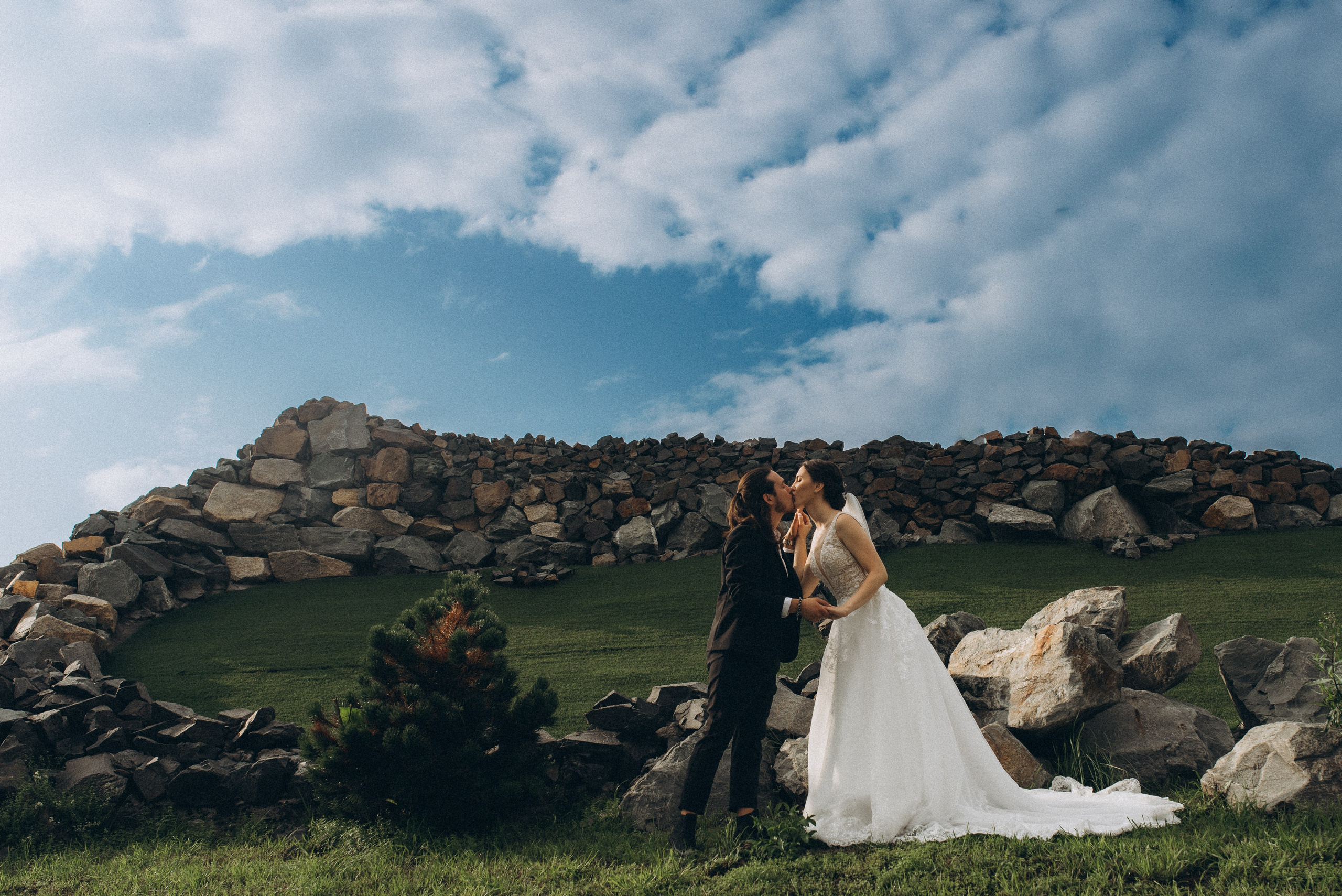 Эпичный кадр поцелуя на фоне монументальной каменной стены под облачным небом.