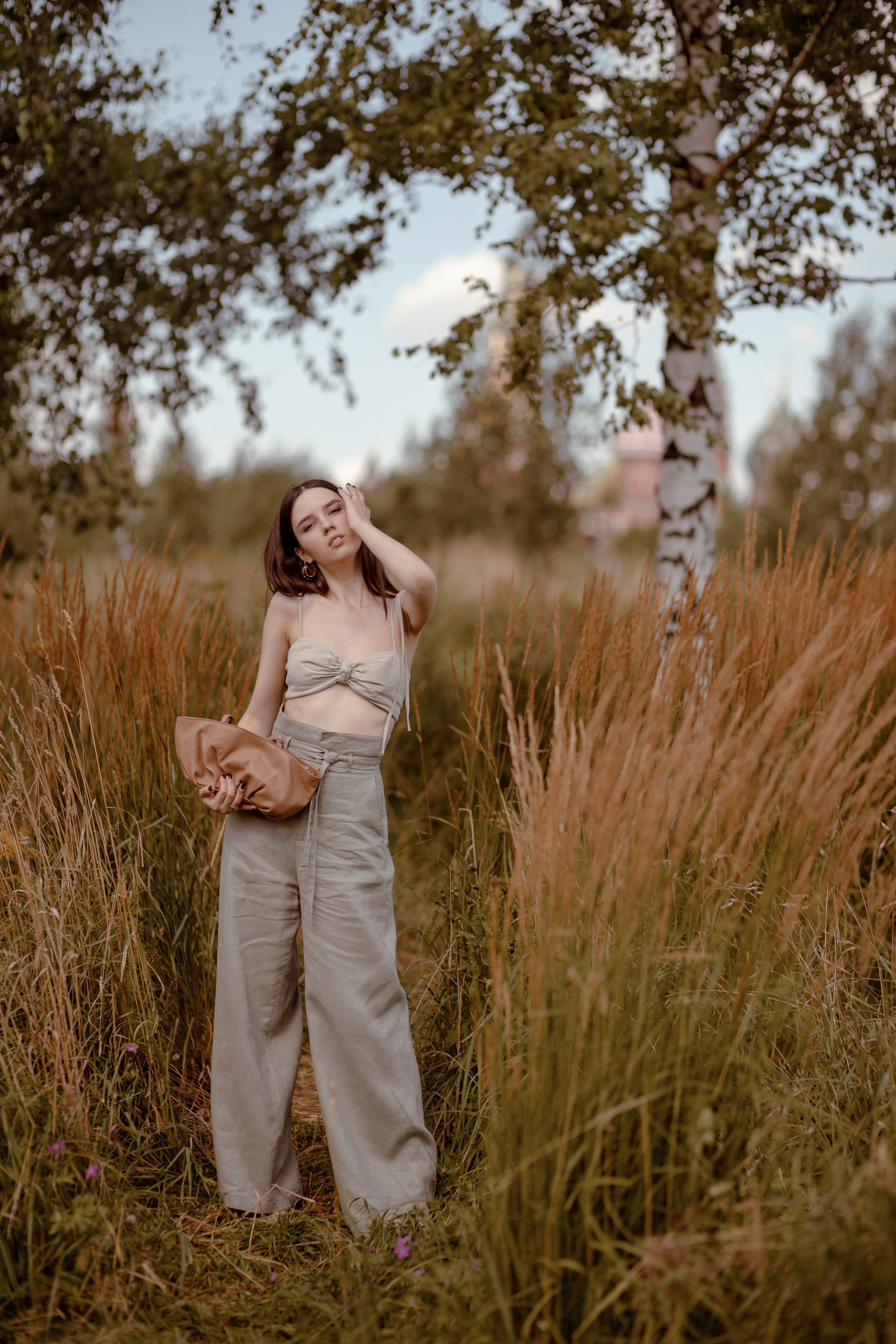  девушка в длинных брюках стоит между берёзами в парке зарядье