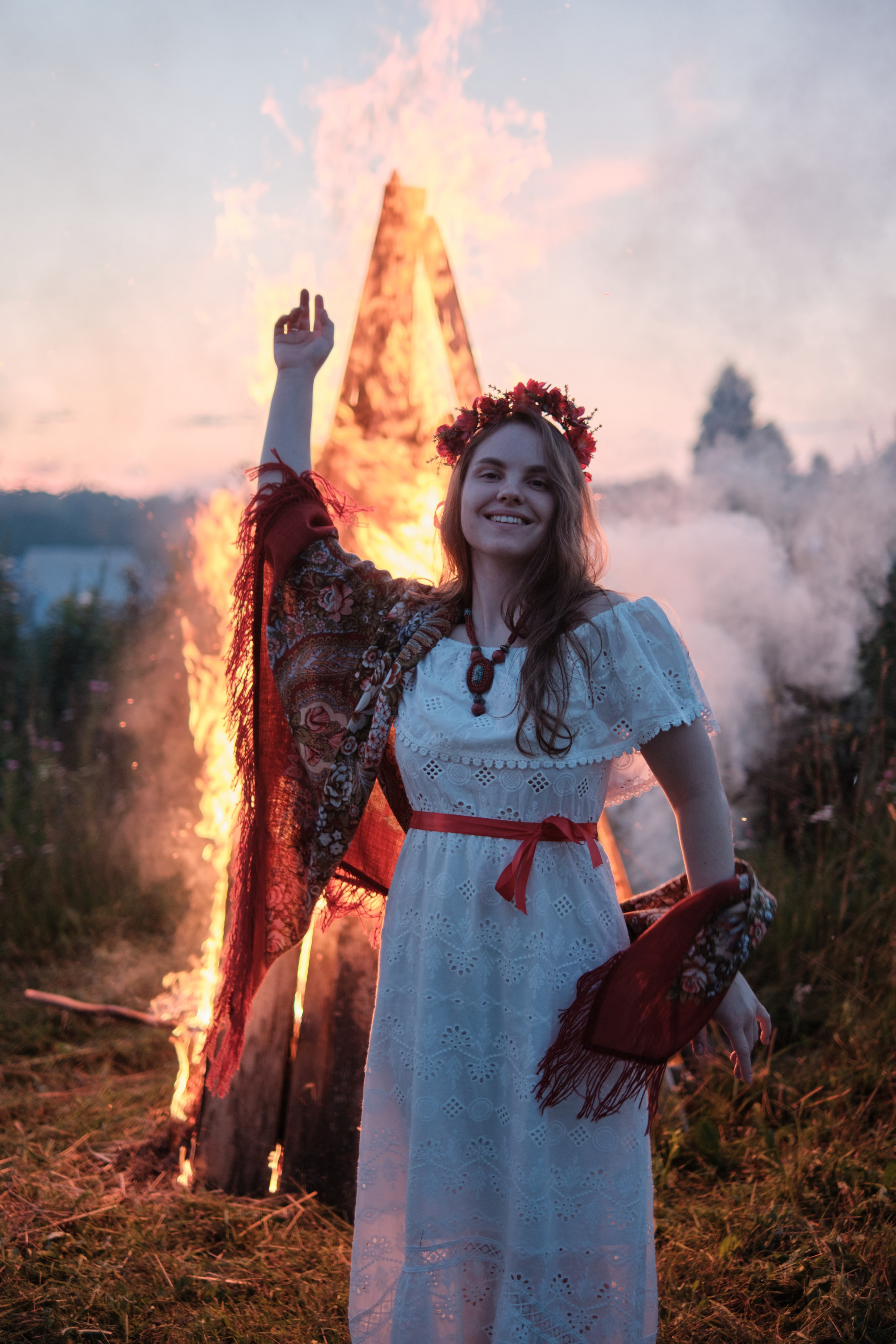 Девушка стоит в русском костюме и венком сзади горит большой костер