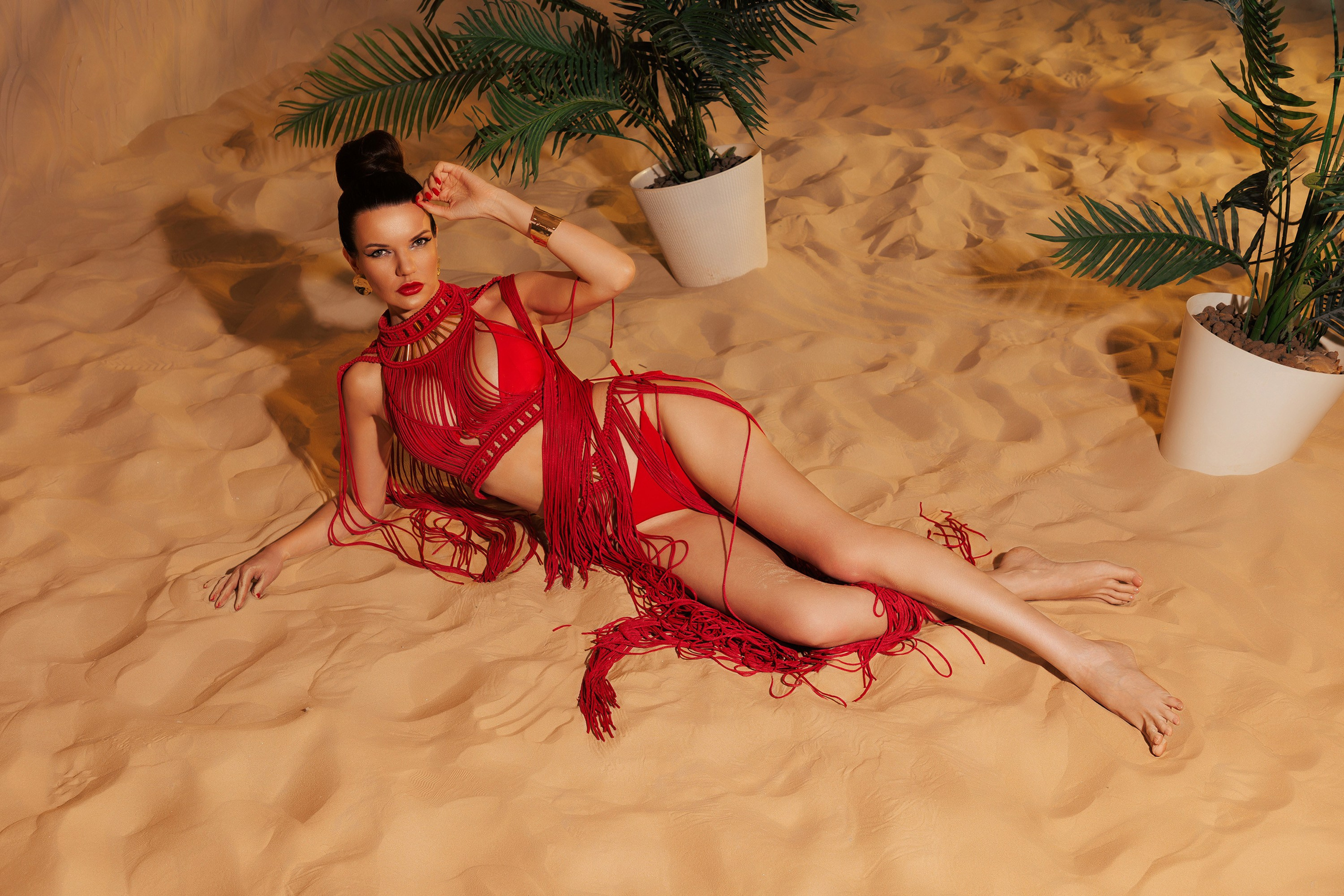 Девушка лежит на песке в красном платье макраме